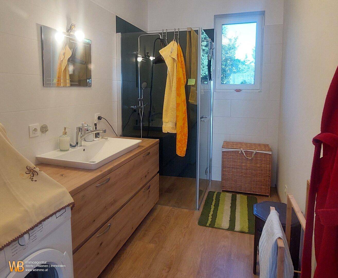 Modernes Badezimmer mit ebenerdiger Dusche, Waschbecken, Holzunterschrank und Fenster.
