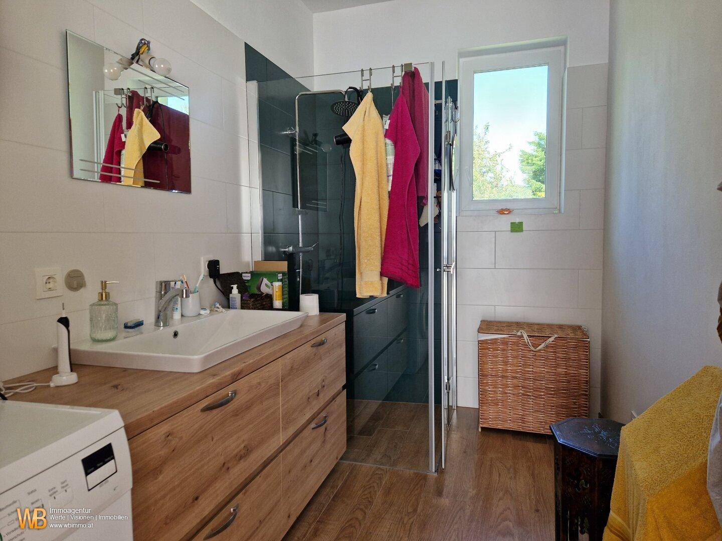 Modernes Badezimmer mit Holzelementen, begehbarer Dusche und Fenster für Tageslicht.