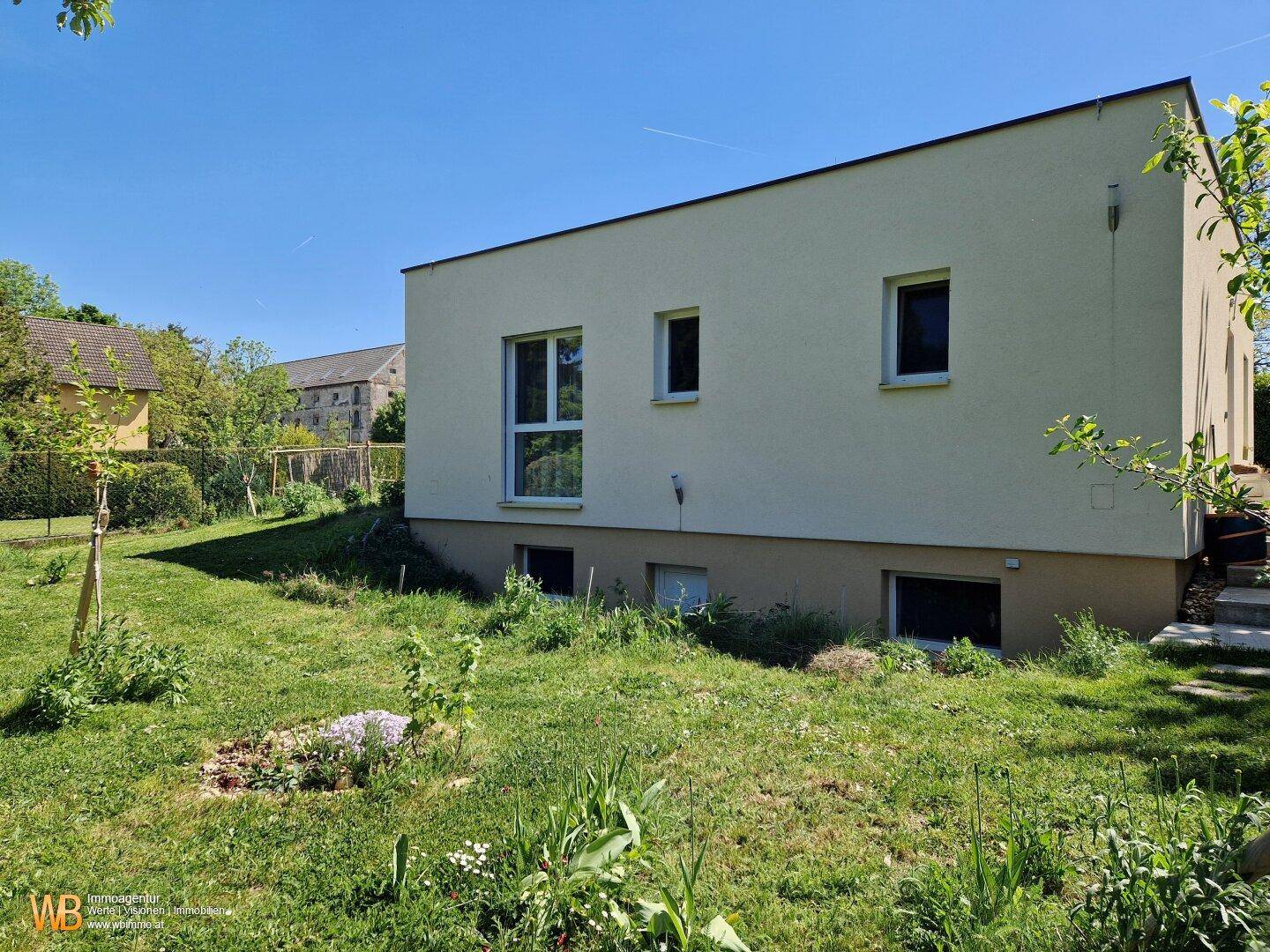 Seitenansicht des modernen Hauses mit großen Fenstern und umliegendem Garten.