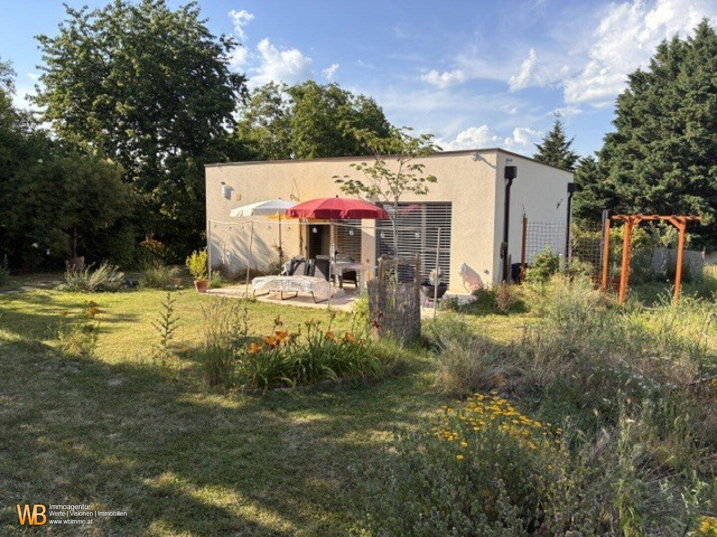 Modernes Haus mit sonnigem Garten und kleiner Terrasse, umgeben von viel Grün.