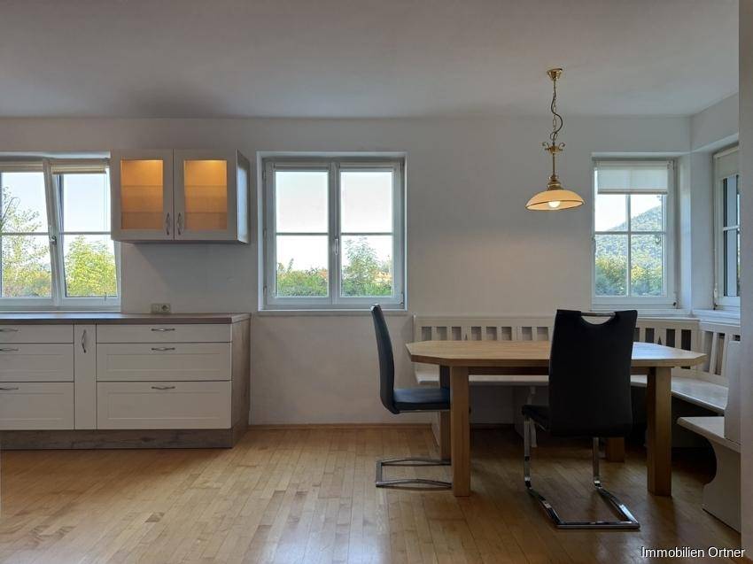 Essbereich mit Holztisch, Sitzbank und Fenstern, die viel Tageslicht hereinlassen.