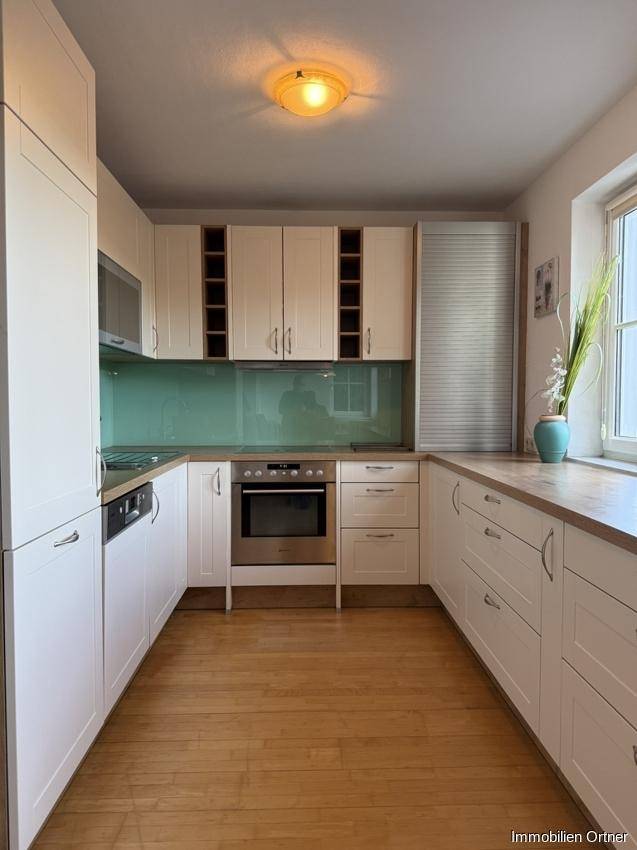 Gut ausgestattete Küche mit weißen Schränken, Holztheke und Fenster für natürliches Licht.