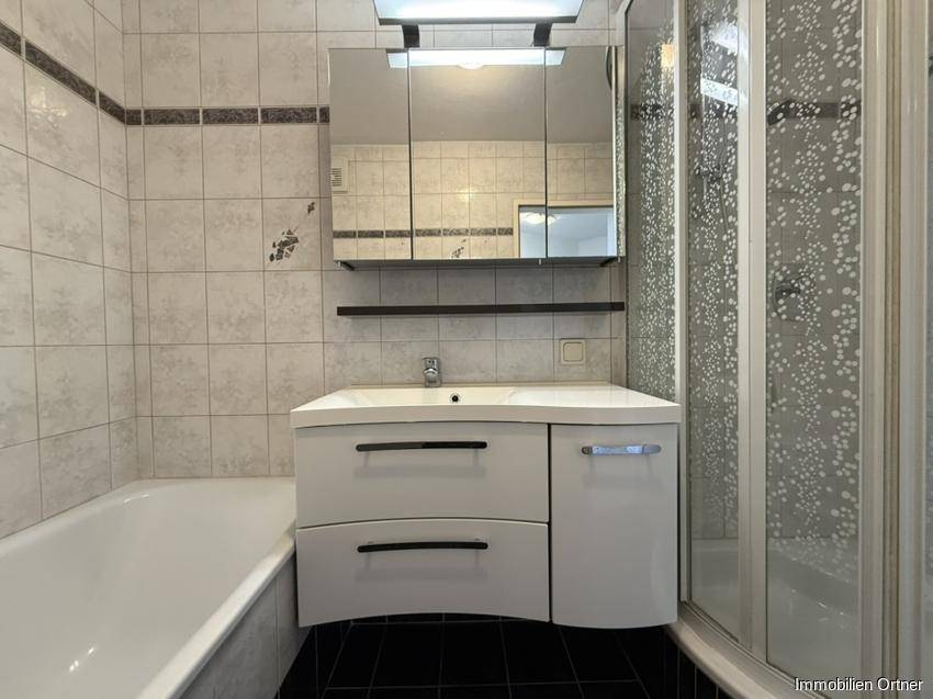 Badezimmer mit Badewanne, Duschkabine, Waschbeckenunterschrank und Spiegelschrank.