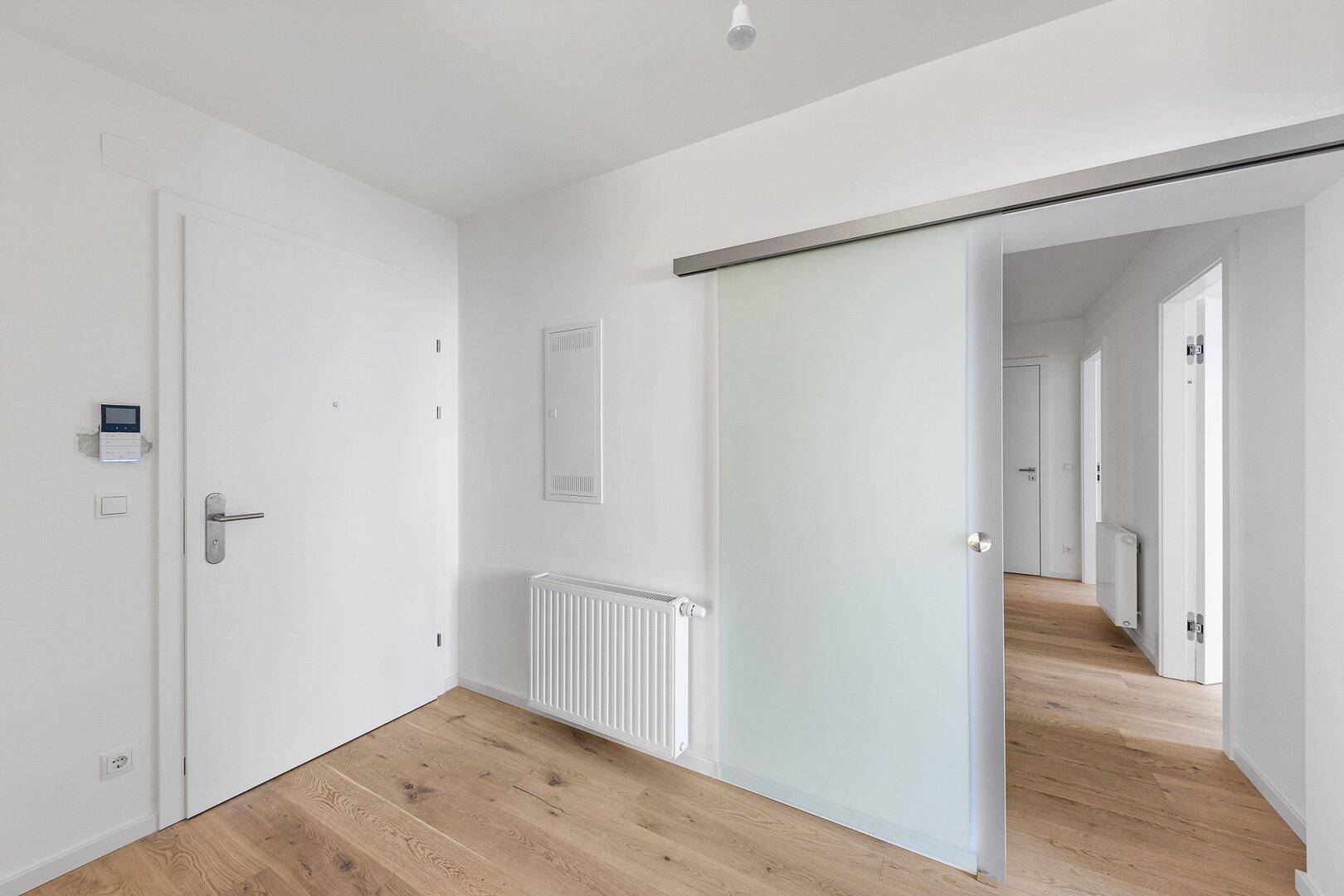 Heller Eingangsbereich mit Holzboden und moderner Schiebetür aus Milchglas.