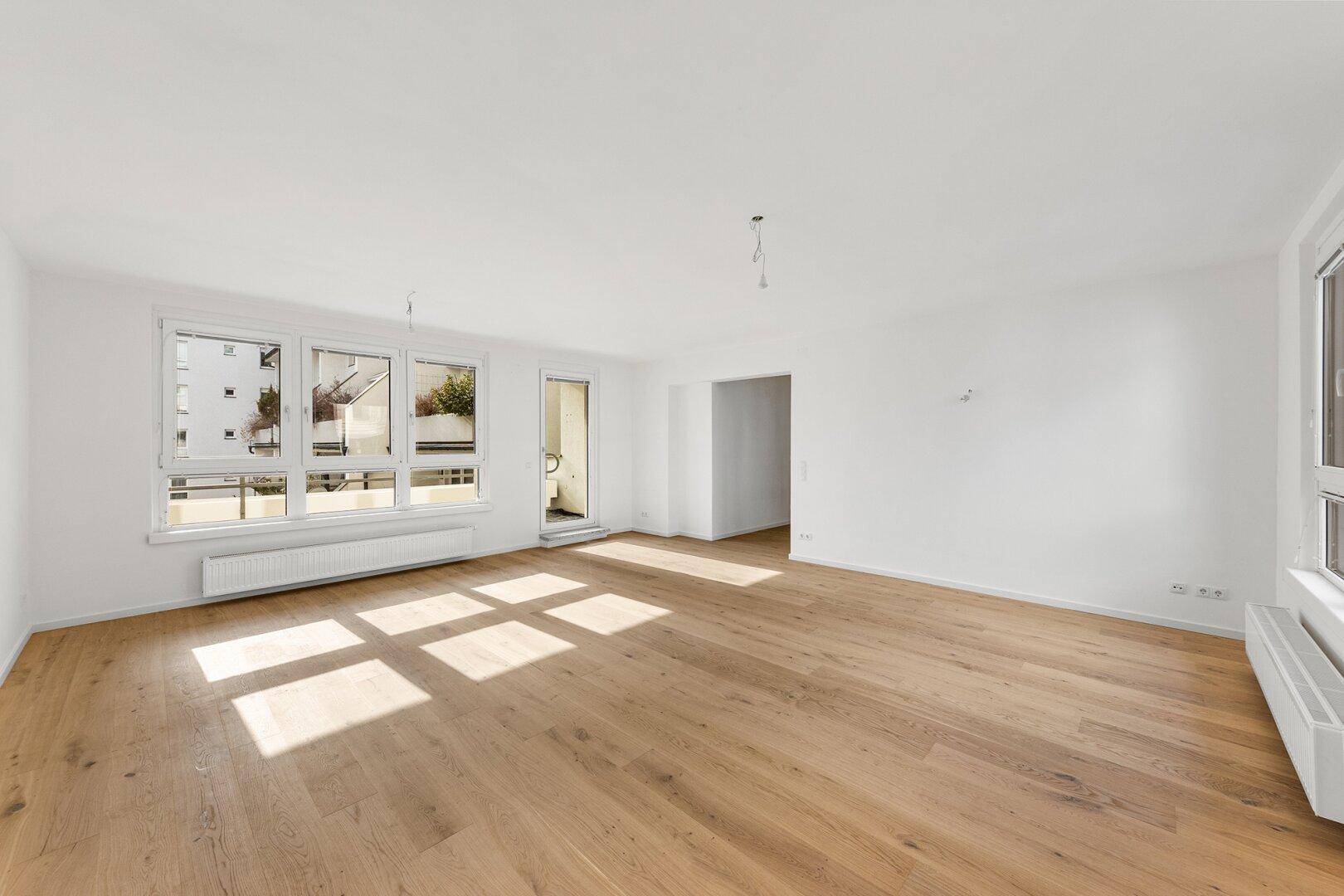 Geräumiges, lichtdurchflutetes Wohnzimmer mit Parkettboden und Zugang zum Balkon.