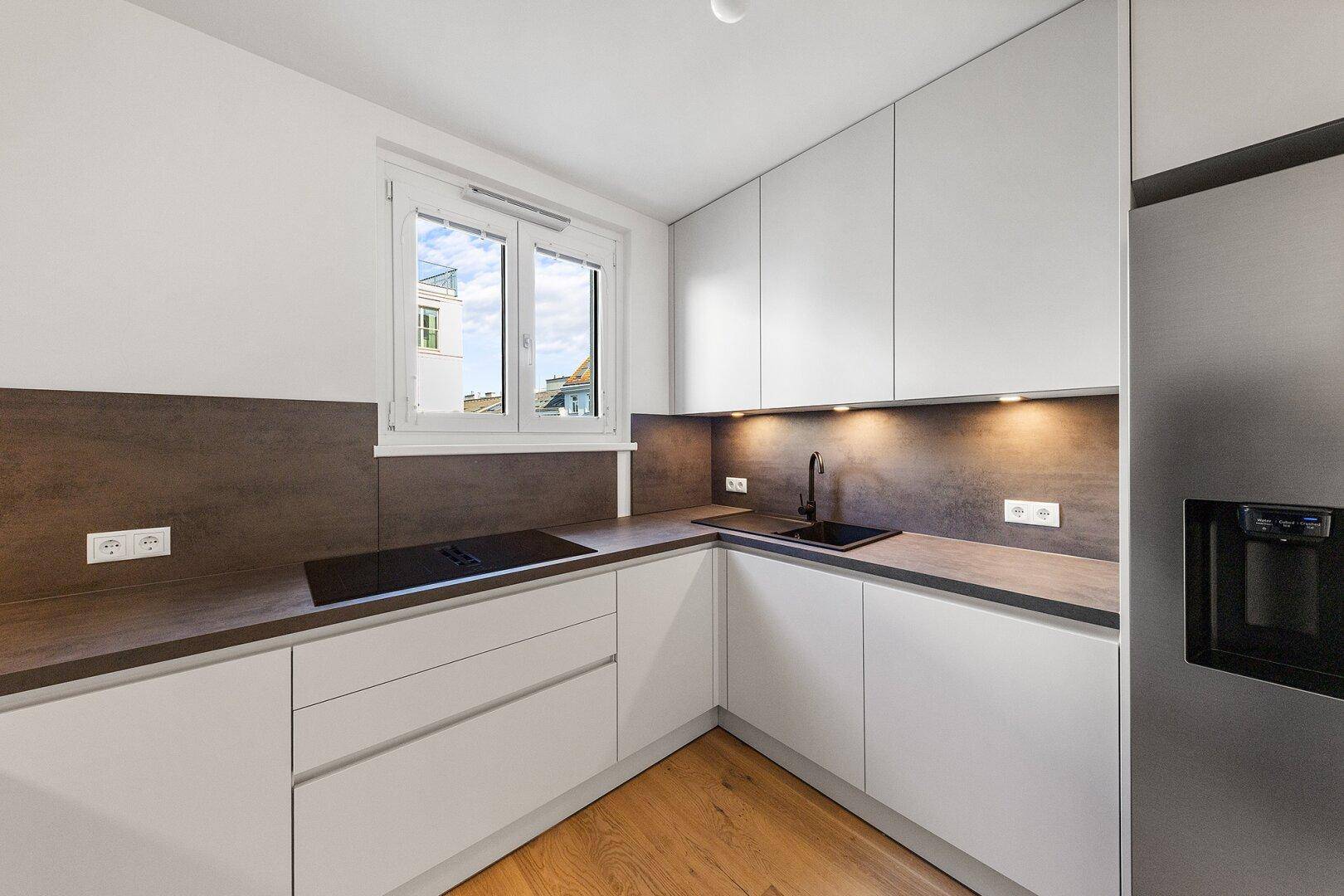 Helle, moderne Küche mit Induktionskochfeld, Spüle und integriertem Kühlschrank.