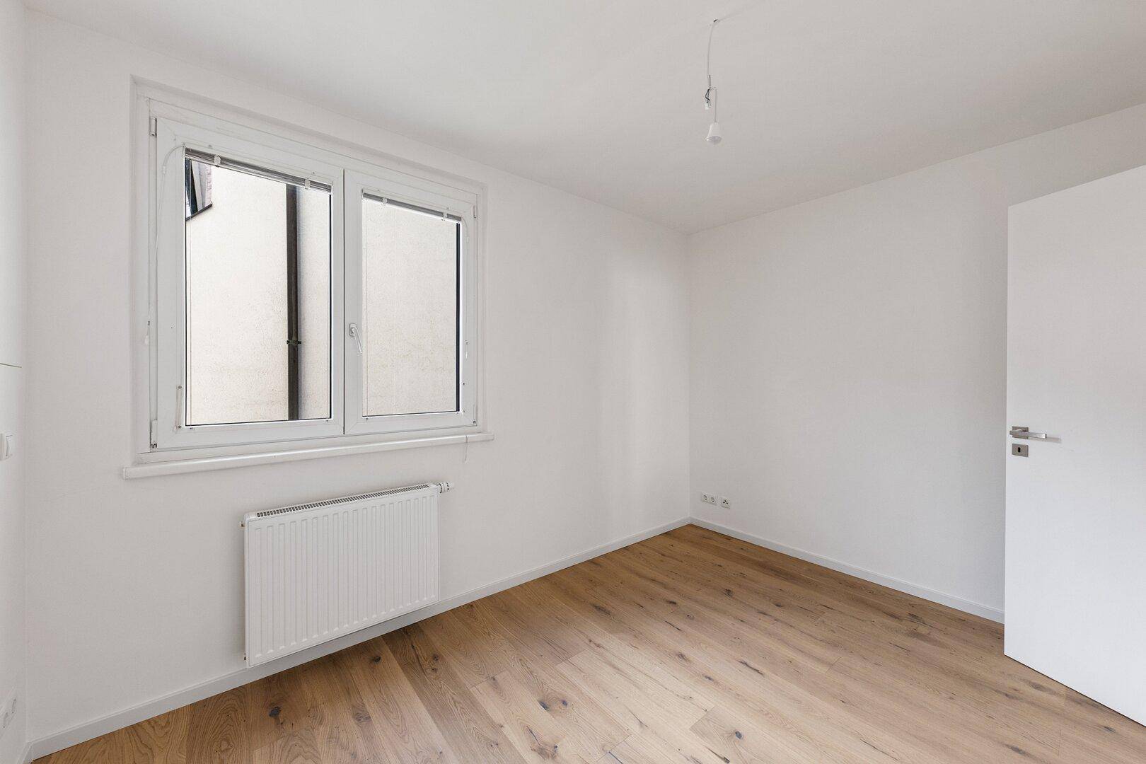 Leeres Schlafzimmer mit Holzboden und Fenster, das viel Licht spendet.