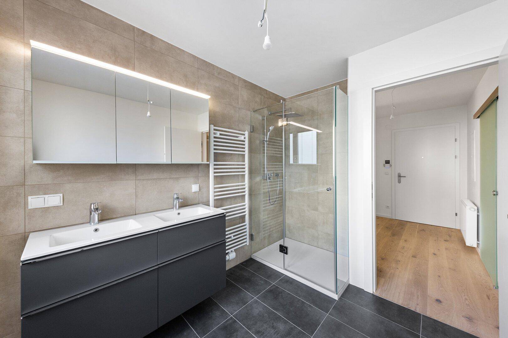 Helles Badezimmer mit begehbarer Dusche, Doppelwaschbecken und beheiztem Handtuchhalter.