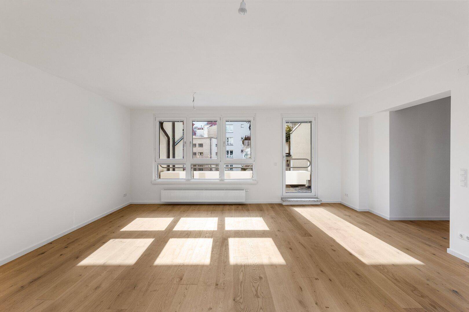 Helles Wohnzimmer mit Holzboden und großen Fenstern, die viel Tageslicht hereinlassen.