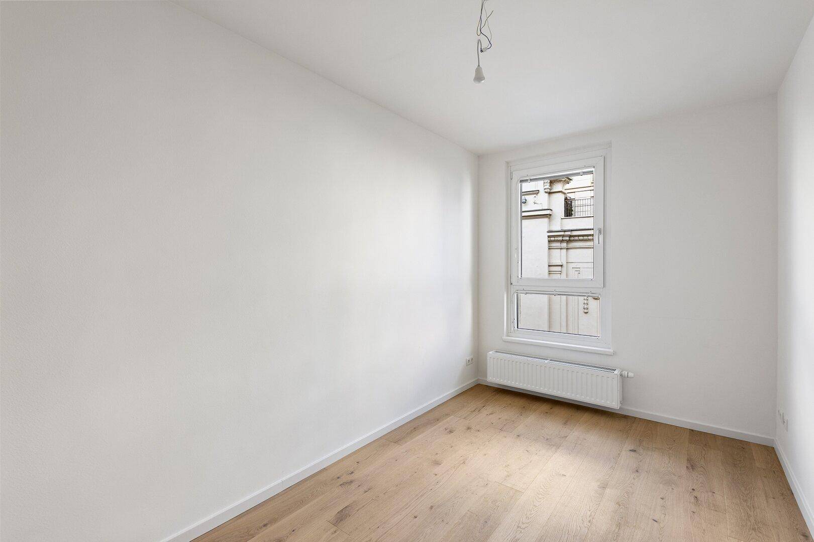Helles Schlafzimmer mit Parkettboden und Blick auf die umliegenden Gebäude.