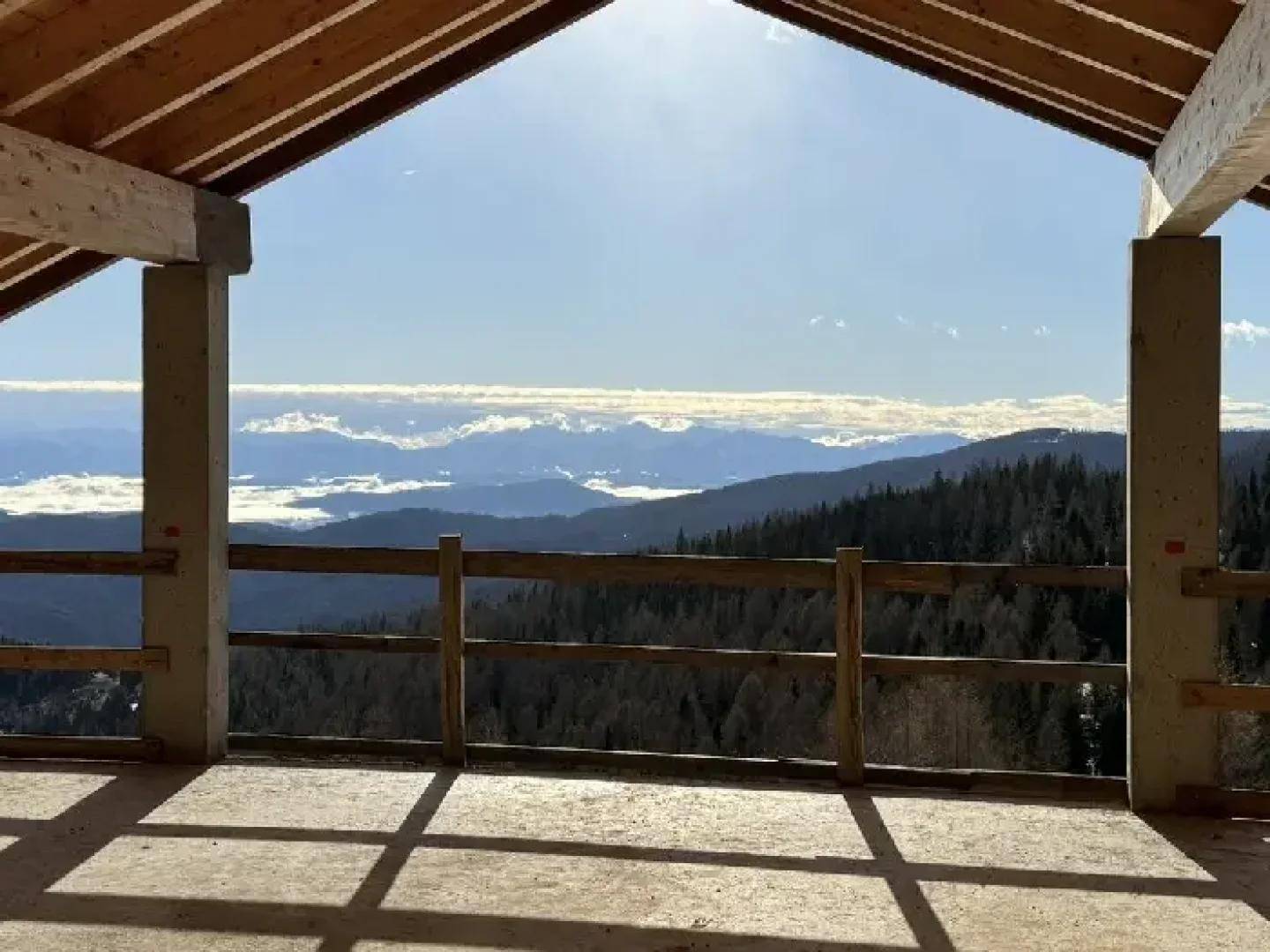 Rustikale Loggia mit Holzdach und Betonboden, die einen weiten Blick auf Berge und Wälder bietet.