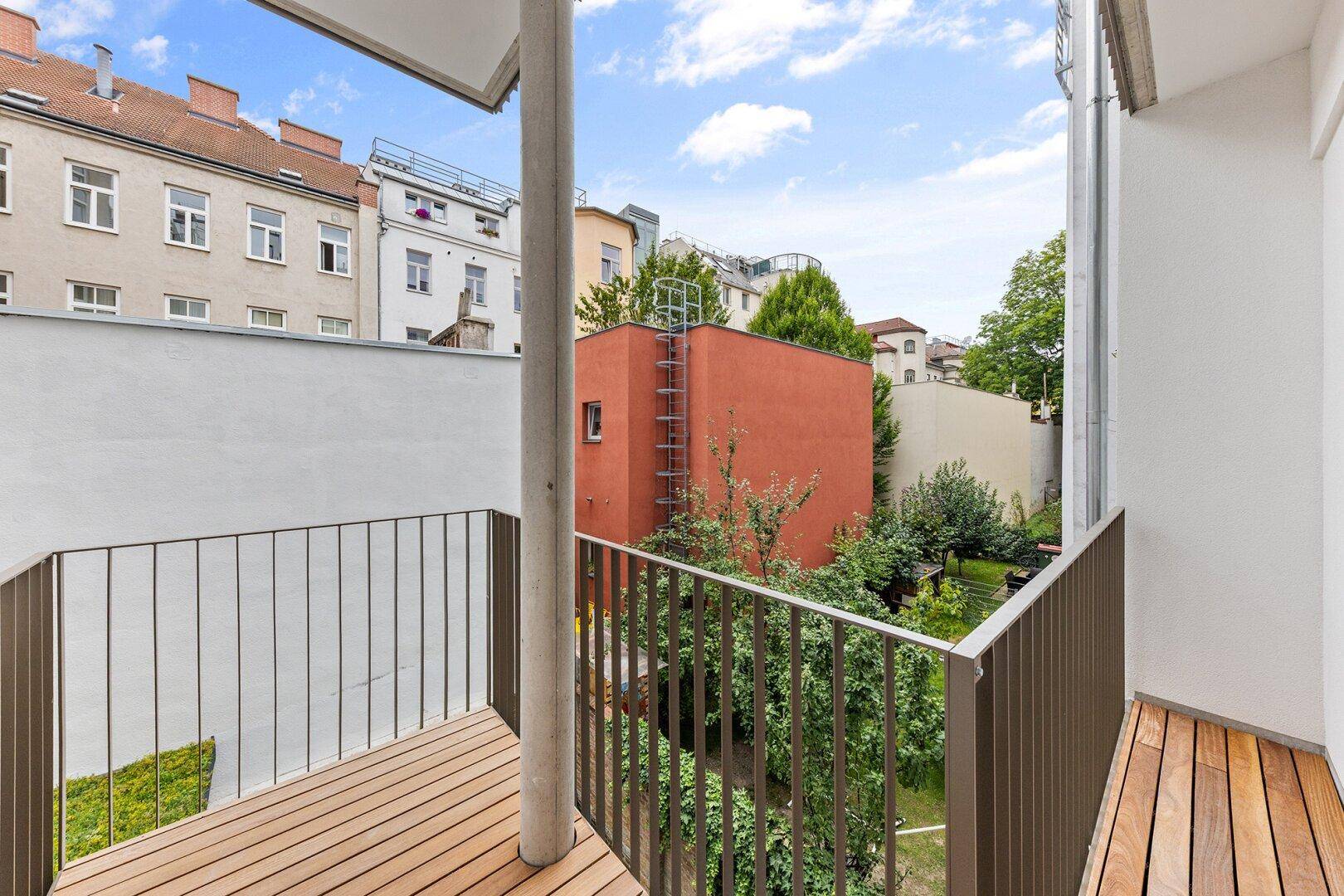 Balkon mit Holzboden und Blick auf den begrünten Innenhof und die umliegenden Gebäude.