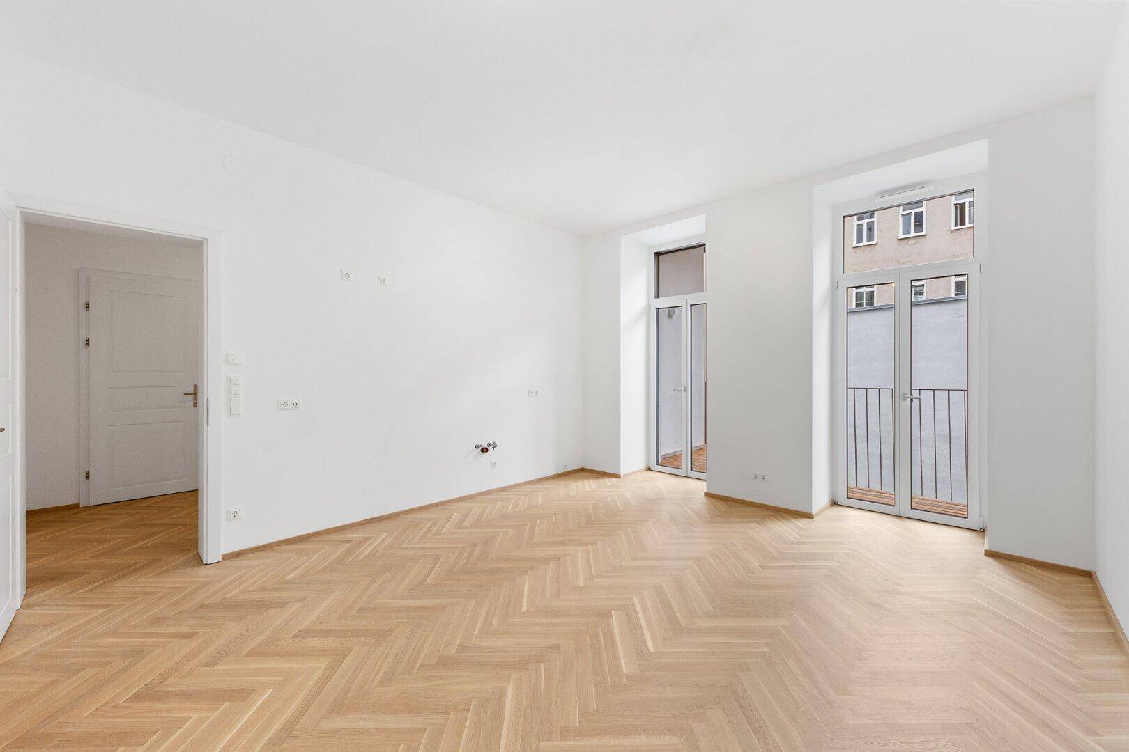 Geräumiges Zimmer mit Fischgrätparkett und zwei französischen Balkonen.
