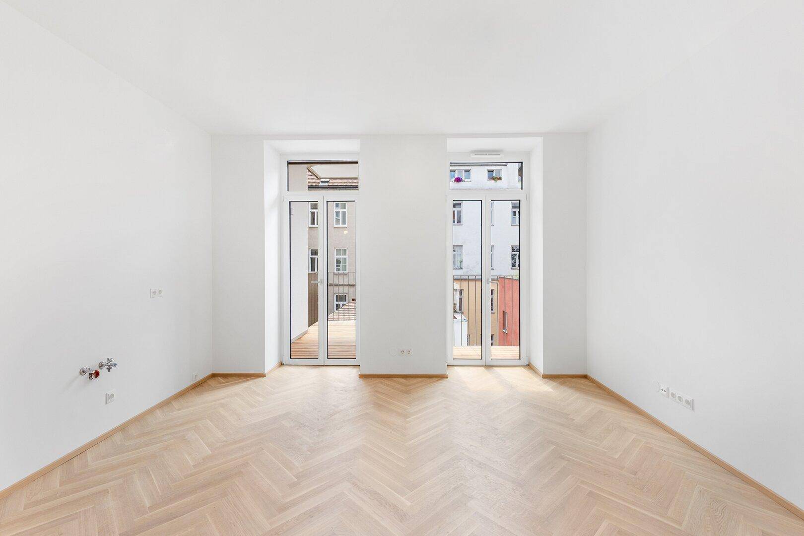Helles Zimmer mit Fischgrätparkett und Zugang zu einem französischen Balkon.