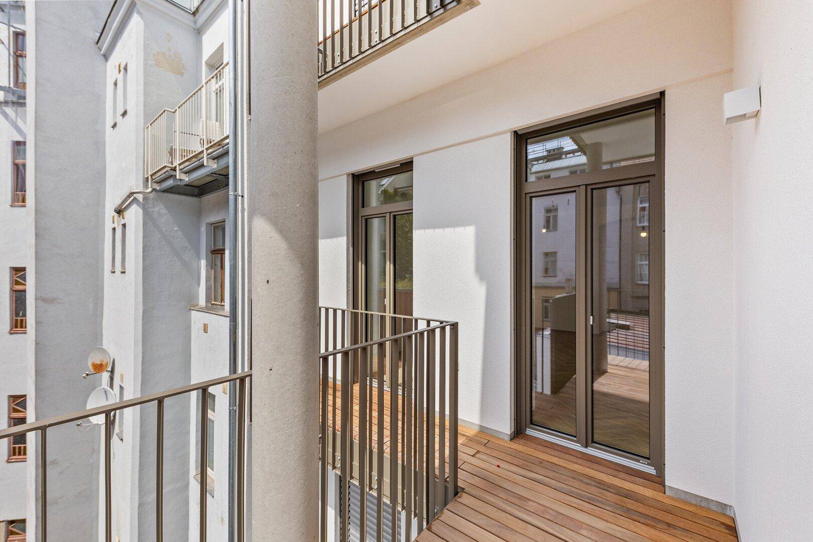 Heller Balkon mit Holzboden und Blick auf den Innenhof, zugänglich von der Wohnung.