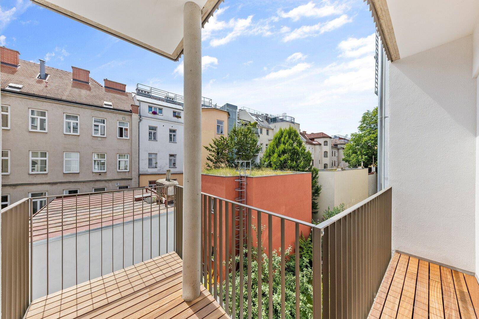 Moderner Balkon mit Holzboden und Metallgeländer, bietet Blick auf den Innenhof.