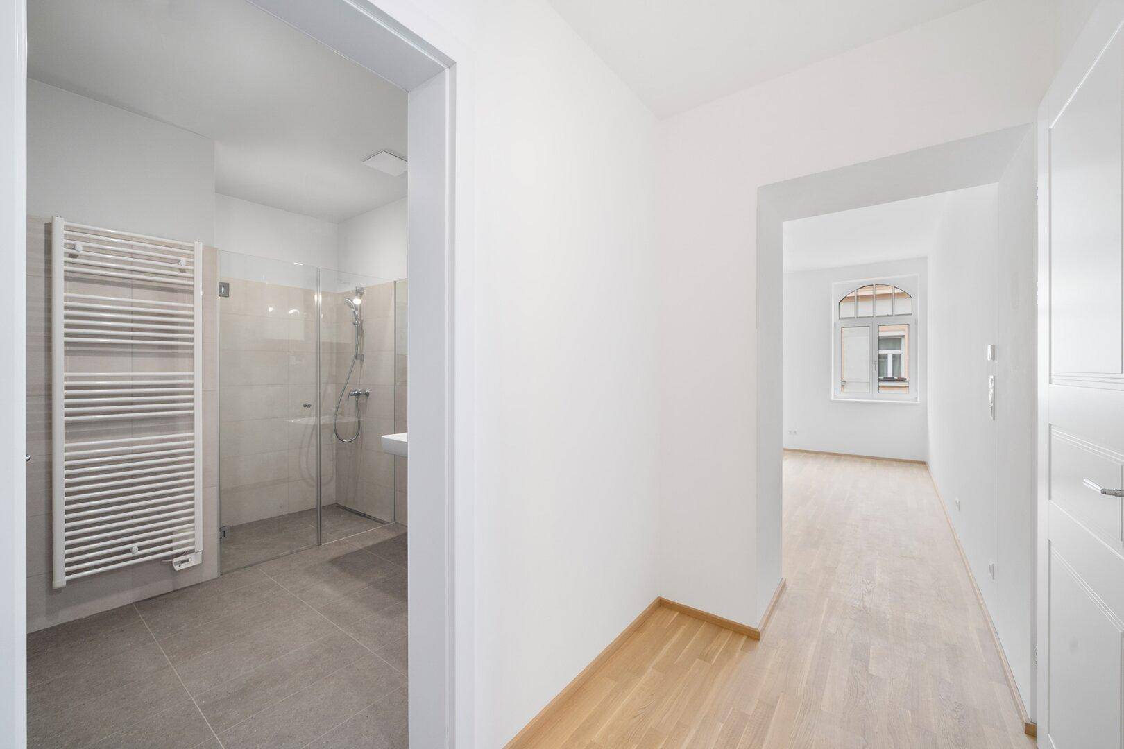 Heller Flur mit Holzfußboden, der zu einem modernen Badezimmer und weiteren Räumen führt.