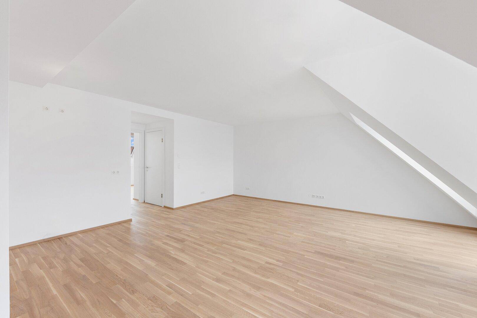 Weitläufiger, leerer Raum im Dachgeschoss mit schrägen Wänden und hellem Parkettboden.