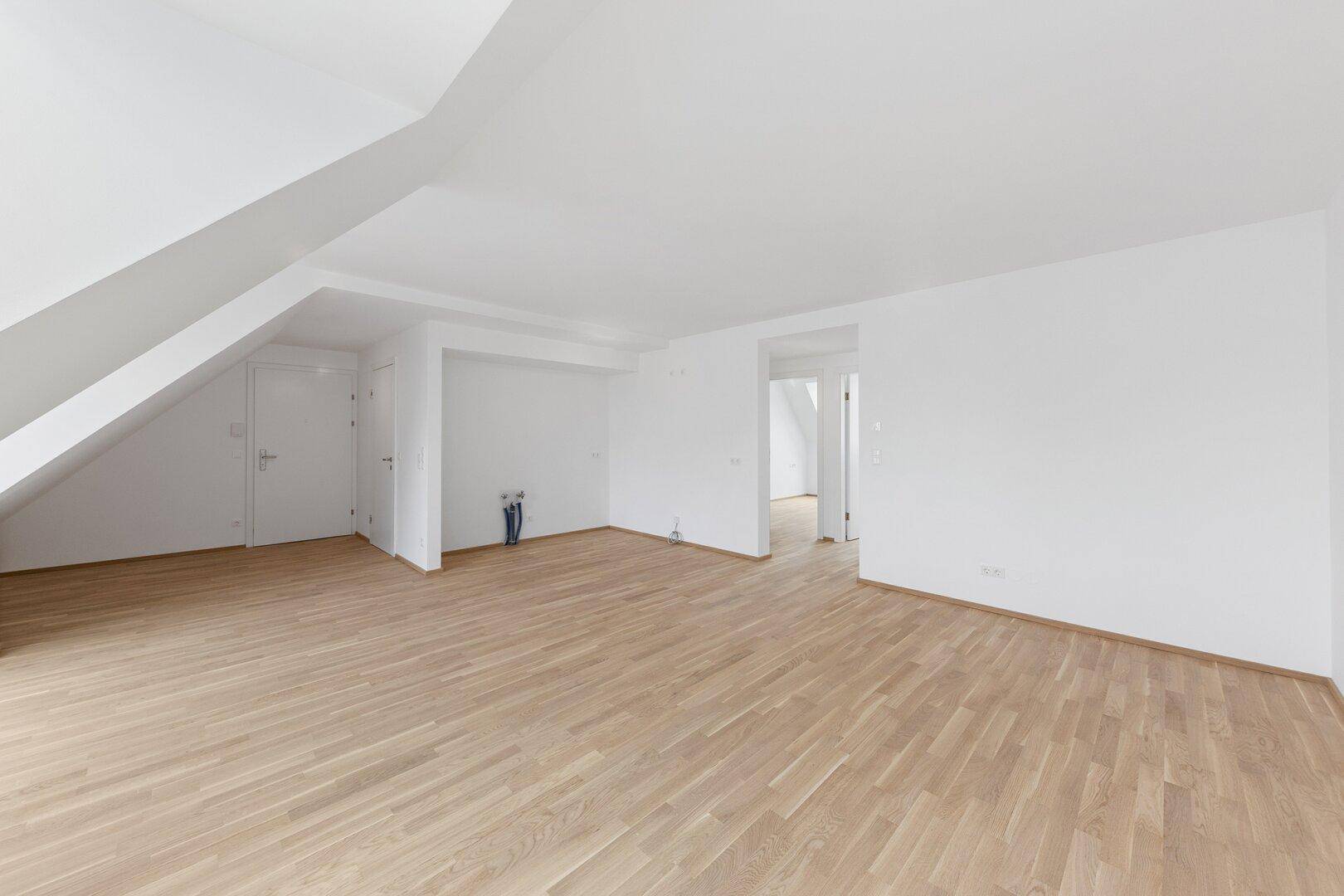 Großzügiger Wohnraum im Dachgeschoss mit hellem Parkettboden und schrägen Wänden.