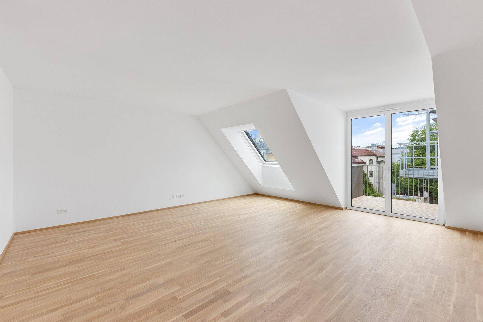 Lichtdurchfluteter Dachgeschossraum mit Zugang zu einem Balkon und hellem Parkettboden.