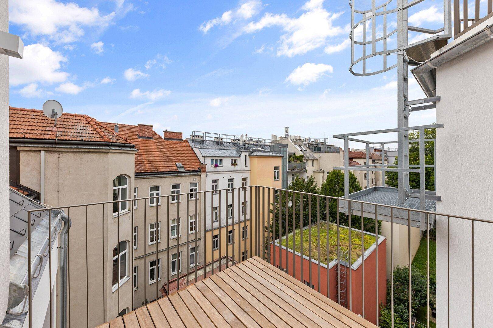 Holzbalkon mit Metallgeländer und weitem Blick über die Dächer der Stadt.
