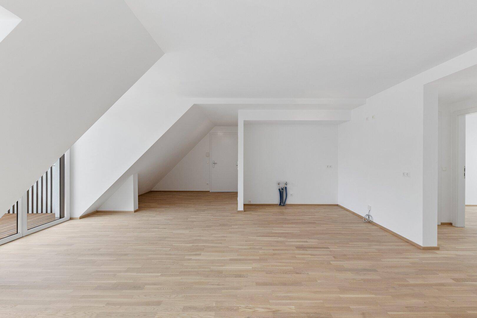 Geräumiger, heller Wohnbereich im Dachgeschoss mit Holzboden und Zugang zum Balkon.