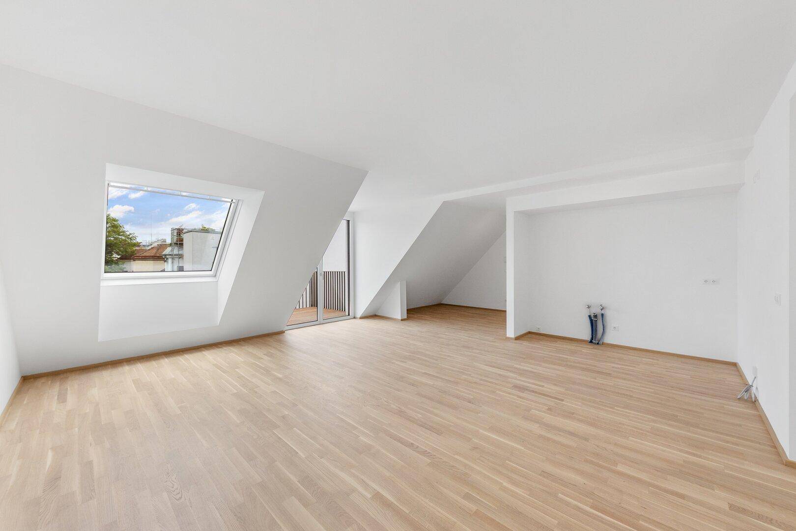 Großer Wohnbereich im Dachgeschoss mit Dachfenster, Balkonzugang und hellem Holzboden.