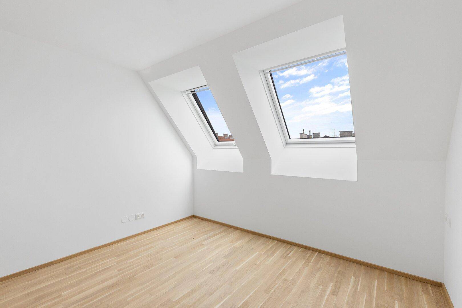 Helles Zimmer im Dachgeschoss mit zwei Dachfenstern und neuem Holzboden.