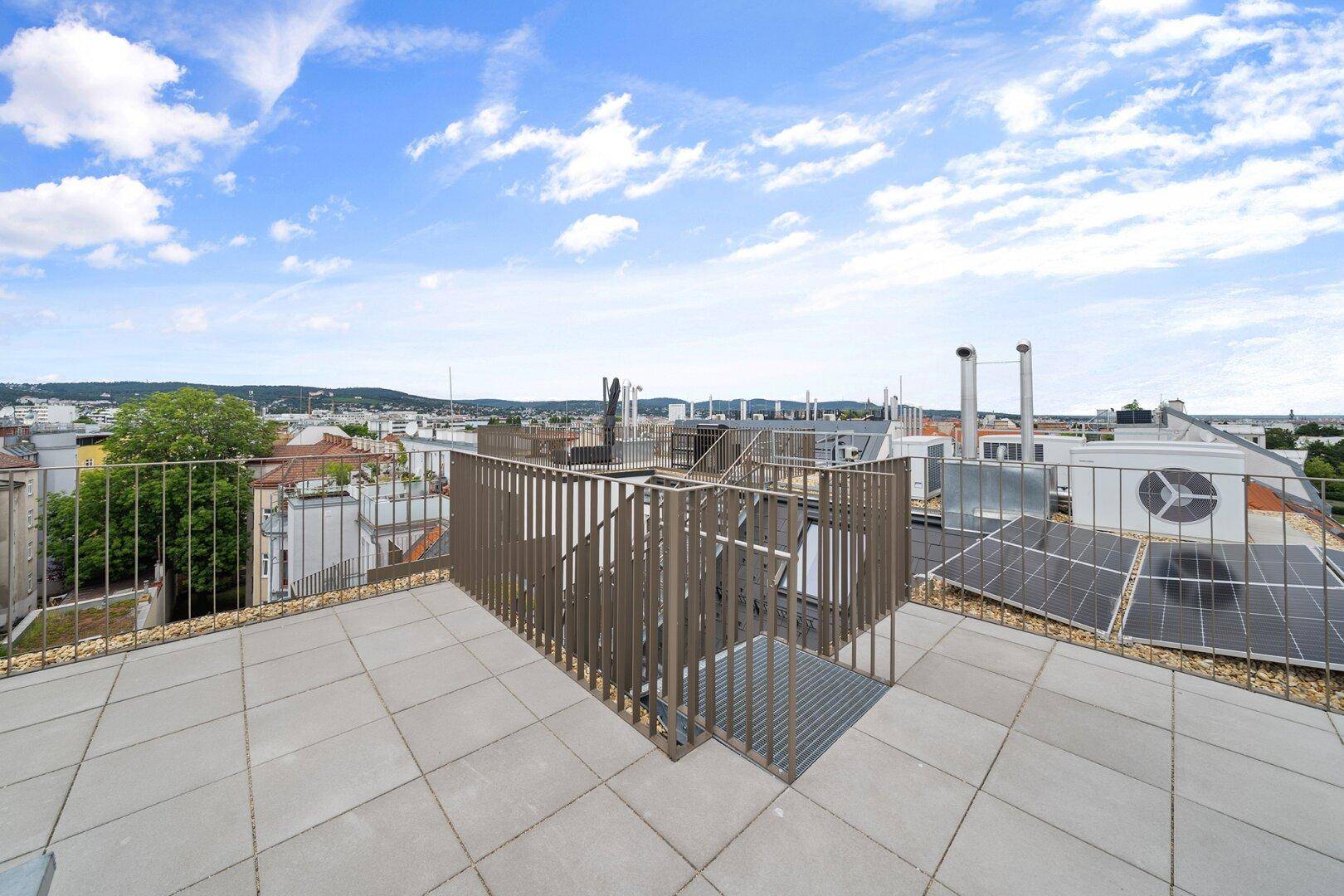 Weitläufige Dachterrasse mit Fliesenboden, Stadtblick und Solaranlage.