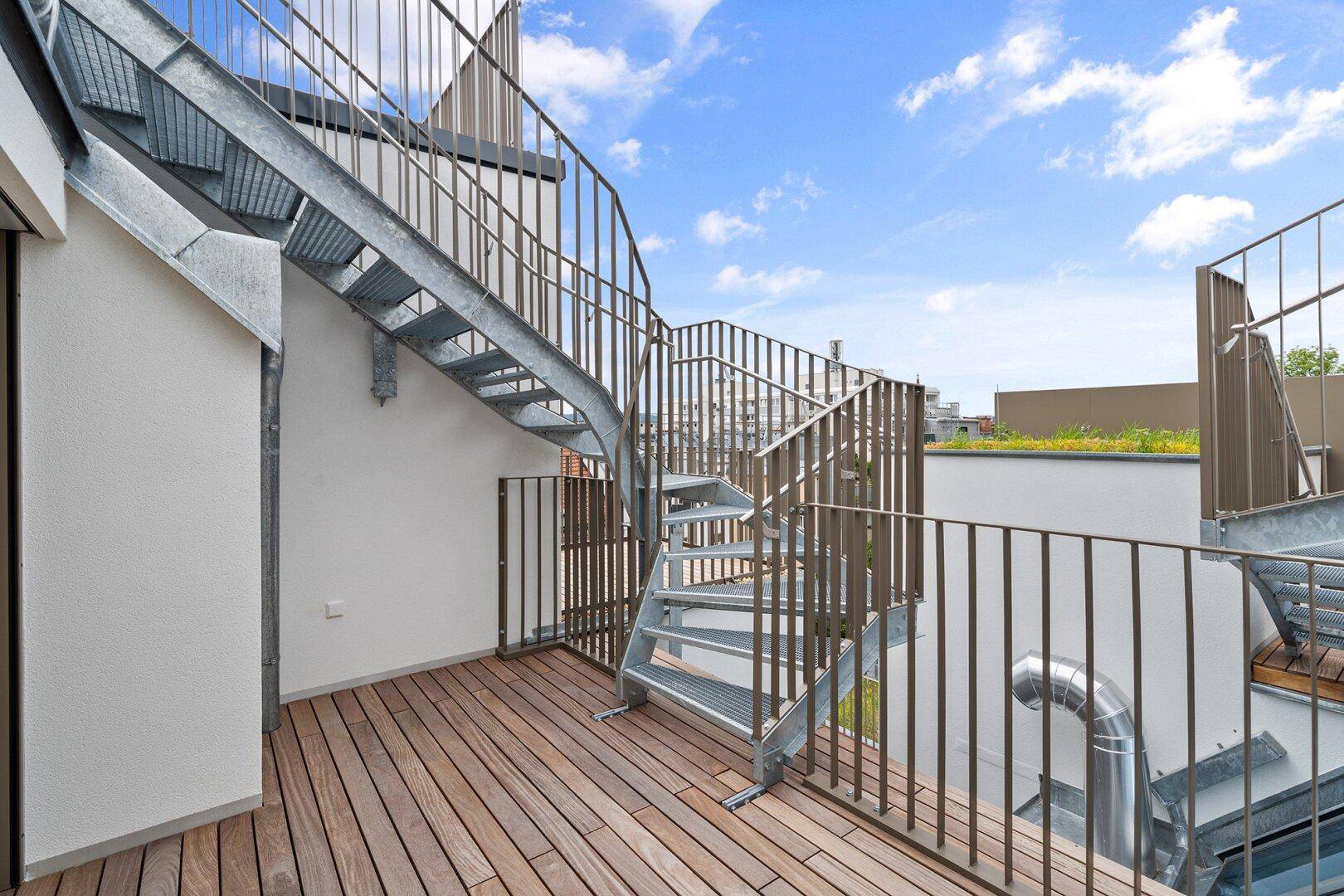 Dachterrasse mit Holzbelag und Metalltreppe, die zu einer weiteren Ebene führt.