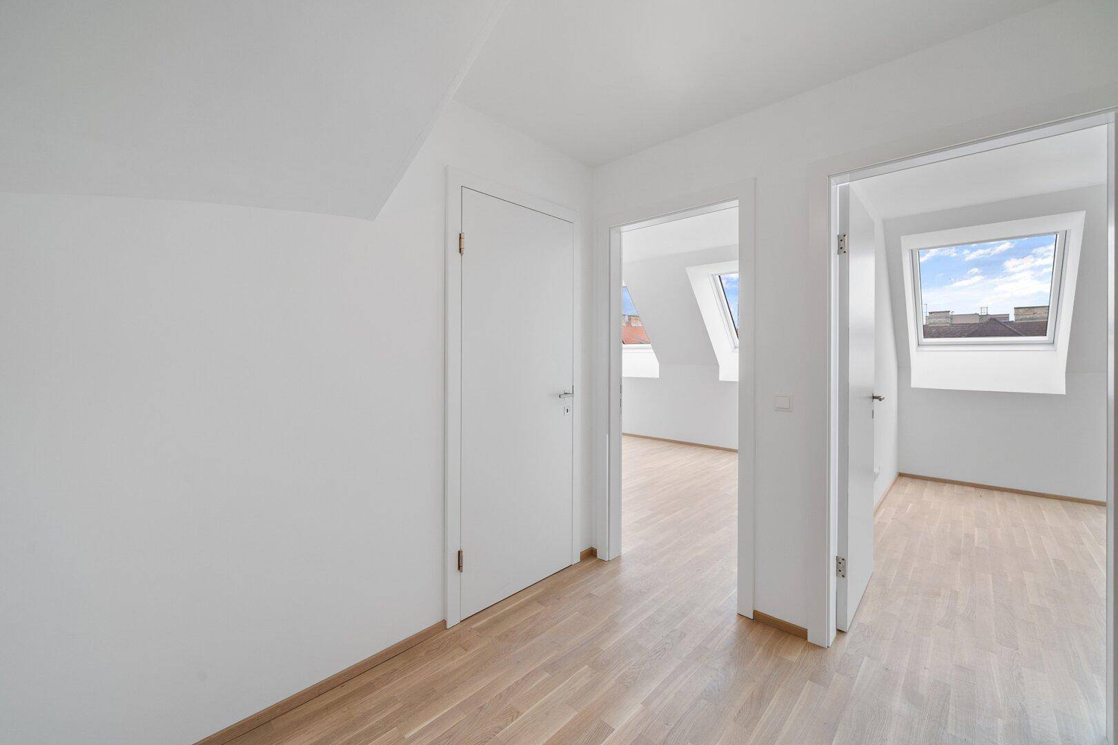 Heller, leerer Raum im Dachgeschoss mit schrägen Wänden, Dachfenstern und hellem Parkettboden.