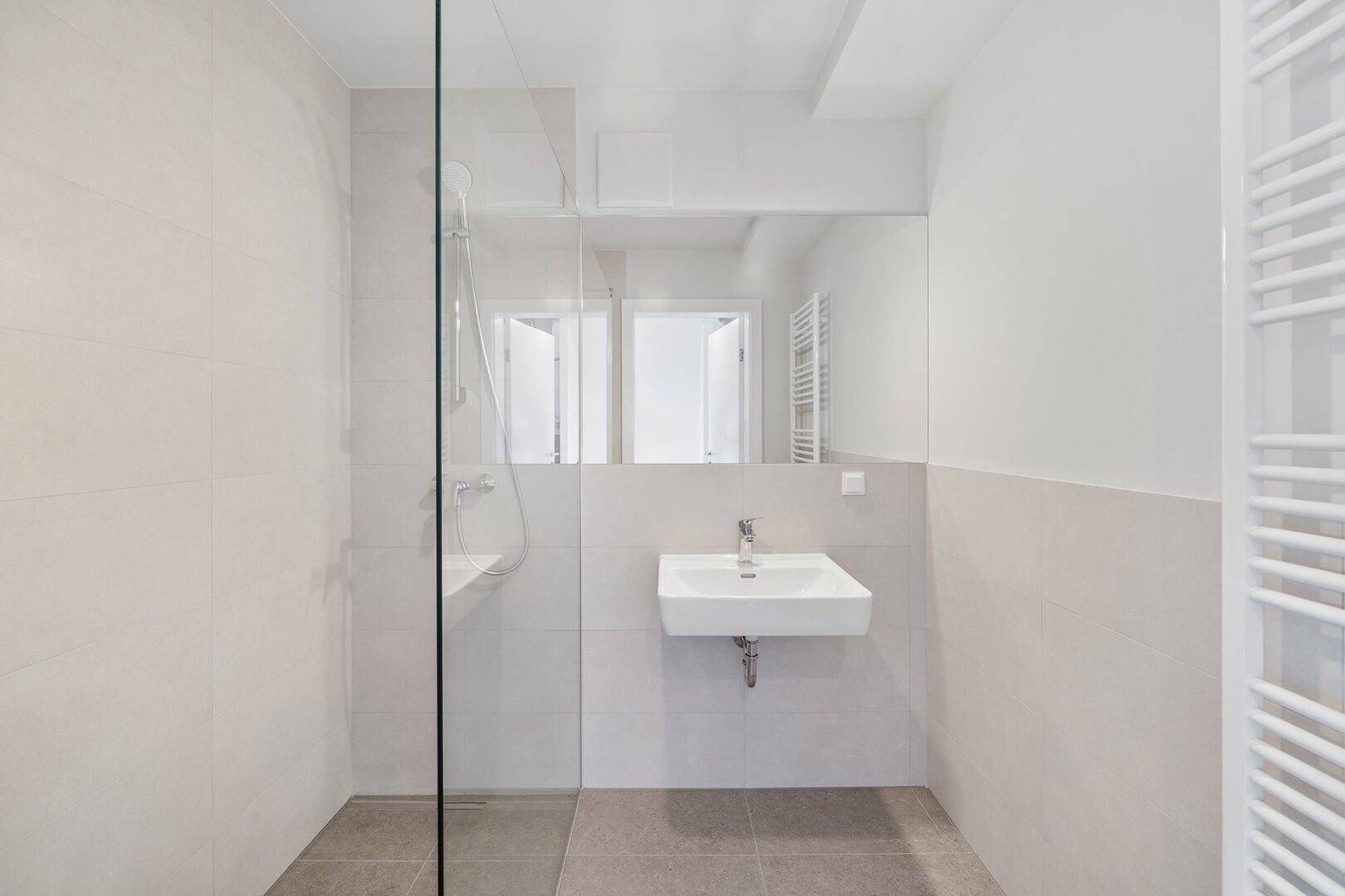 Modernes Badezimmer mit ebenerdiger Dusche, Wandwaschbecken und beheiztem Handtuchhalter.