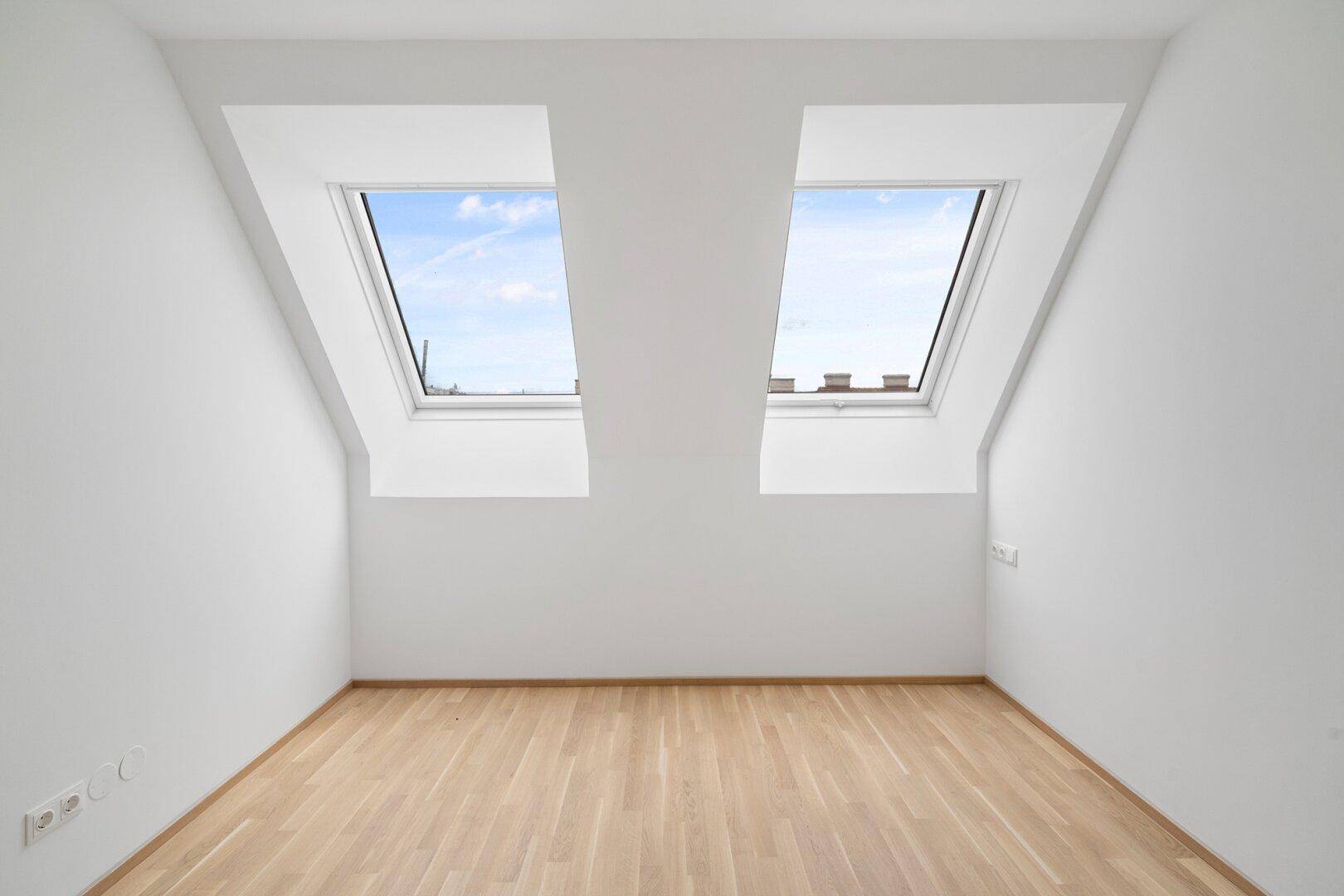 Lichtdurchfluteter Dachgeschossraum mit zwei großen Dachfenstern und hellem Holzparkettboden.