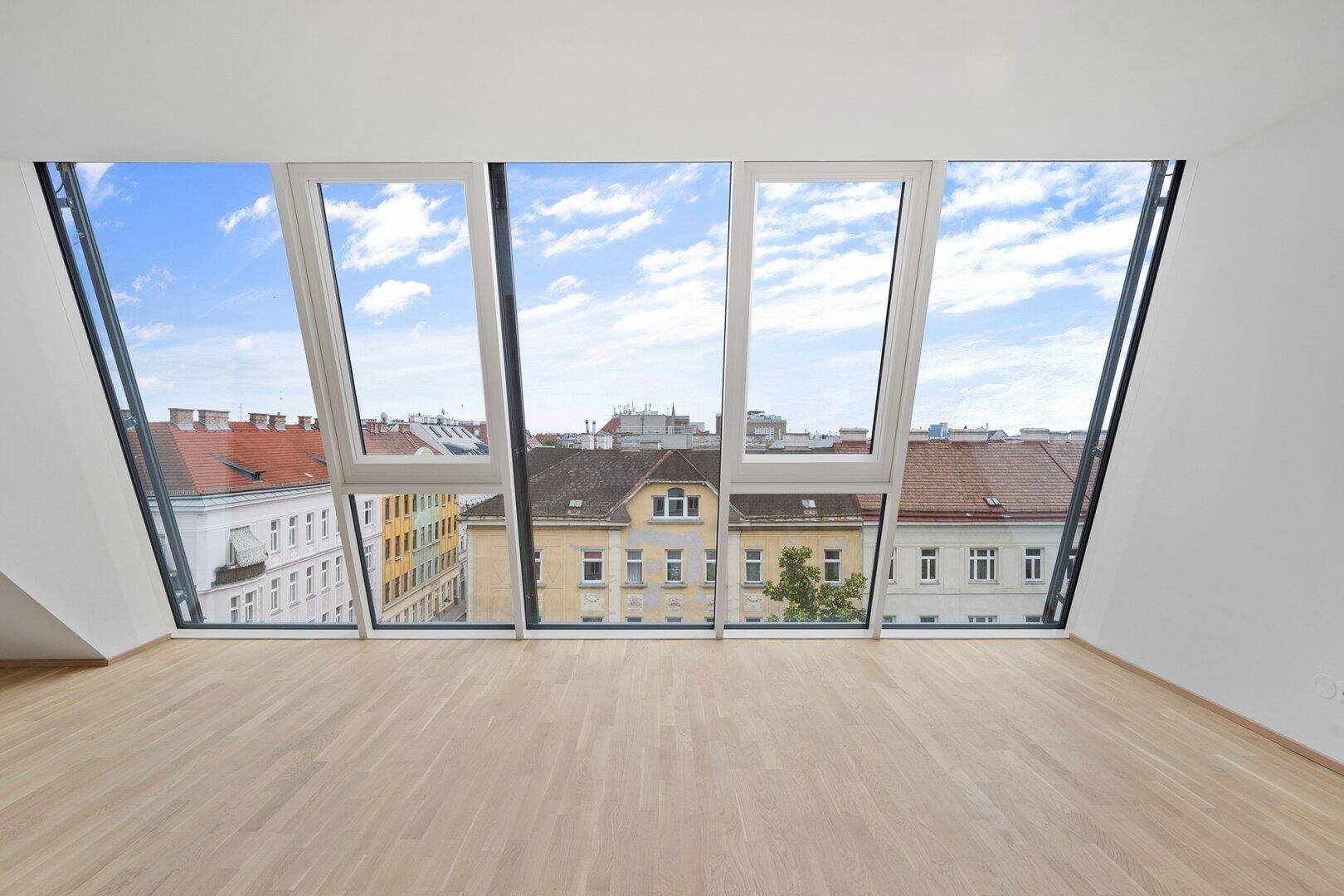 Lichtdurchfluteter Wohnbereich mit großen, schrägen Fenstern und weitem Stadtblick.
