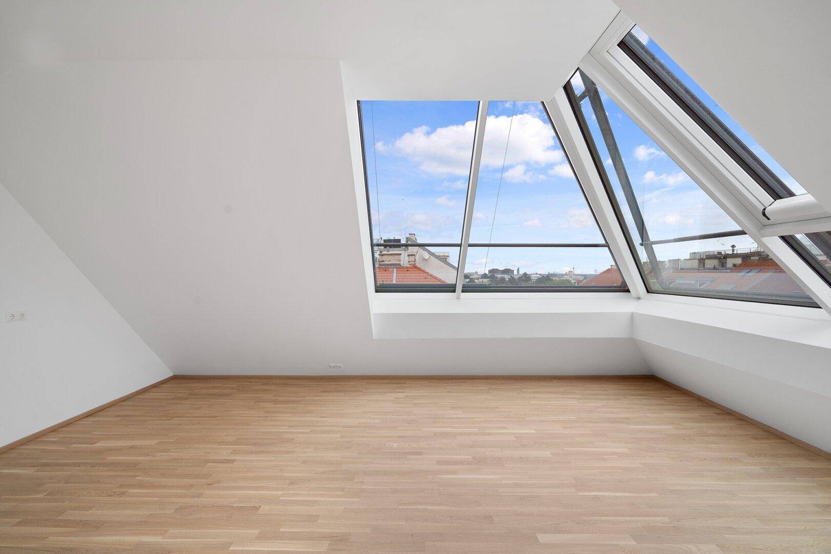 Geräumiger Dachgeschossraum mit großen Fenstern und weitem Blick über die Stadt.