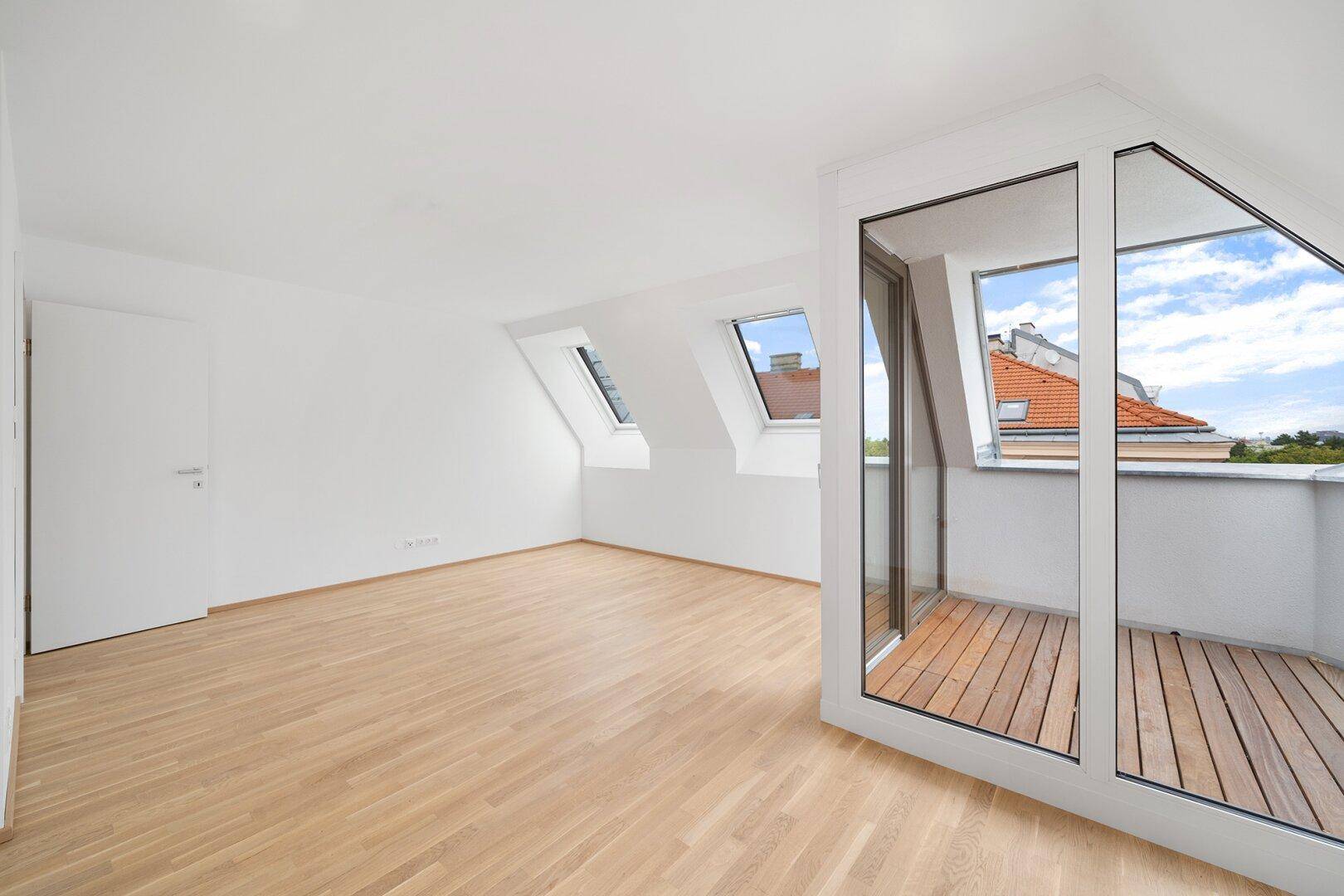 Geräumiges Dachzimmer mit Holzboden, weißen Wänden und Zugang zu einer Loggia.