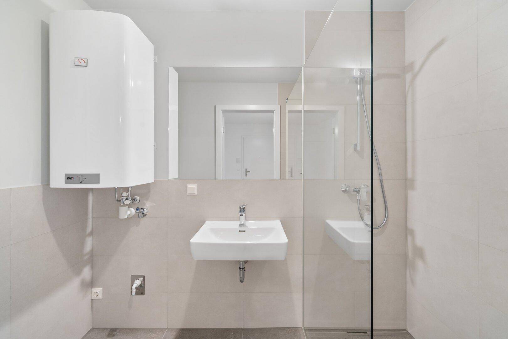 Modernes Badezimmer mit Duschkabine, Waschbecken und Wandspiegel in hellen Farben.