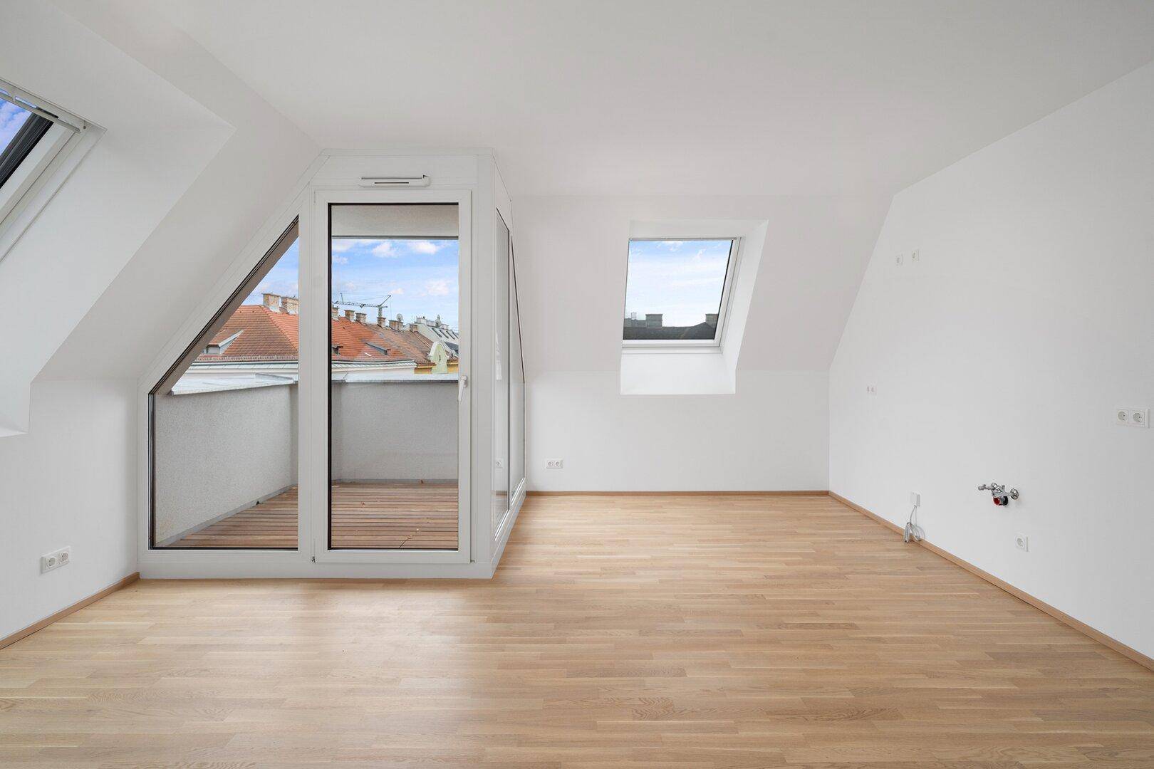 Helles Dachzimmer mit Holzboden und Zugang zu einer kleinen Loggia mit Holzdielen.