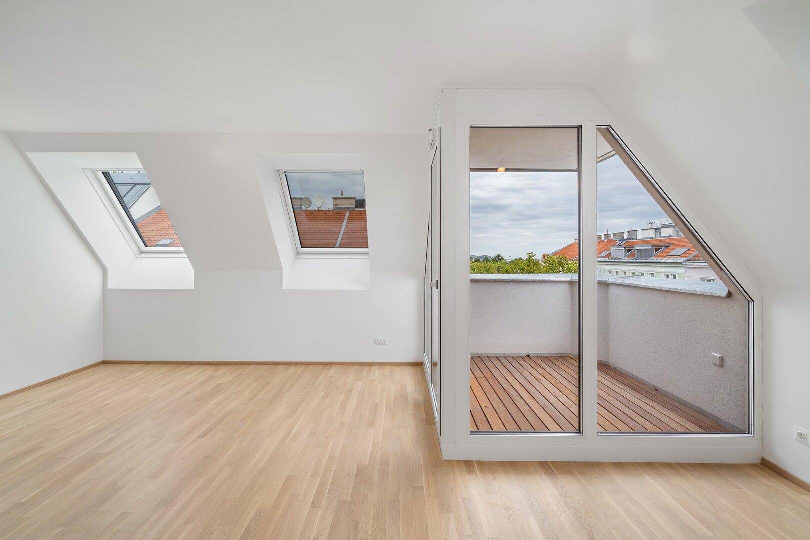 Lichtdurchflutetes Dachzimmer mit Holzboden, Dachfenstern und einer Loggia mit Weitblick.
