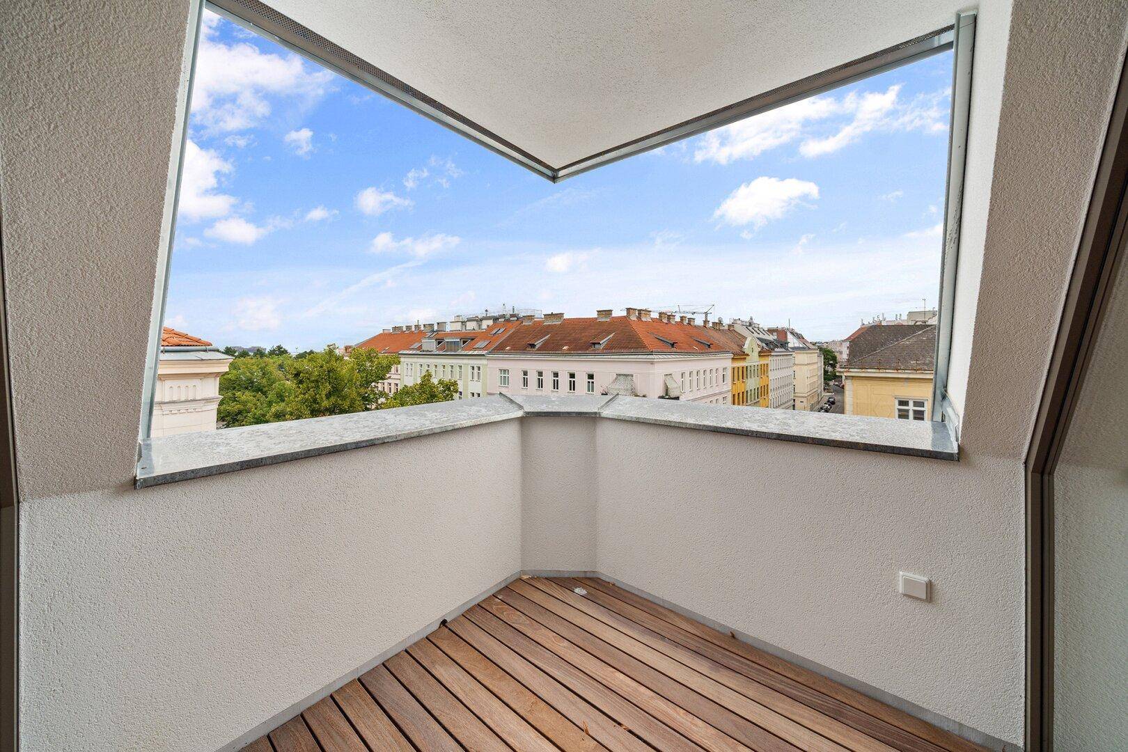 Eck-Loggia mit Holzboden und weitem Blick über die umliegenden Gebäude und den Himmel.