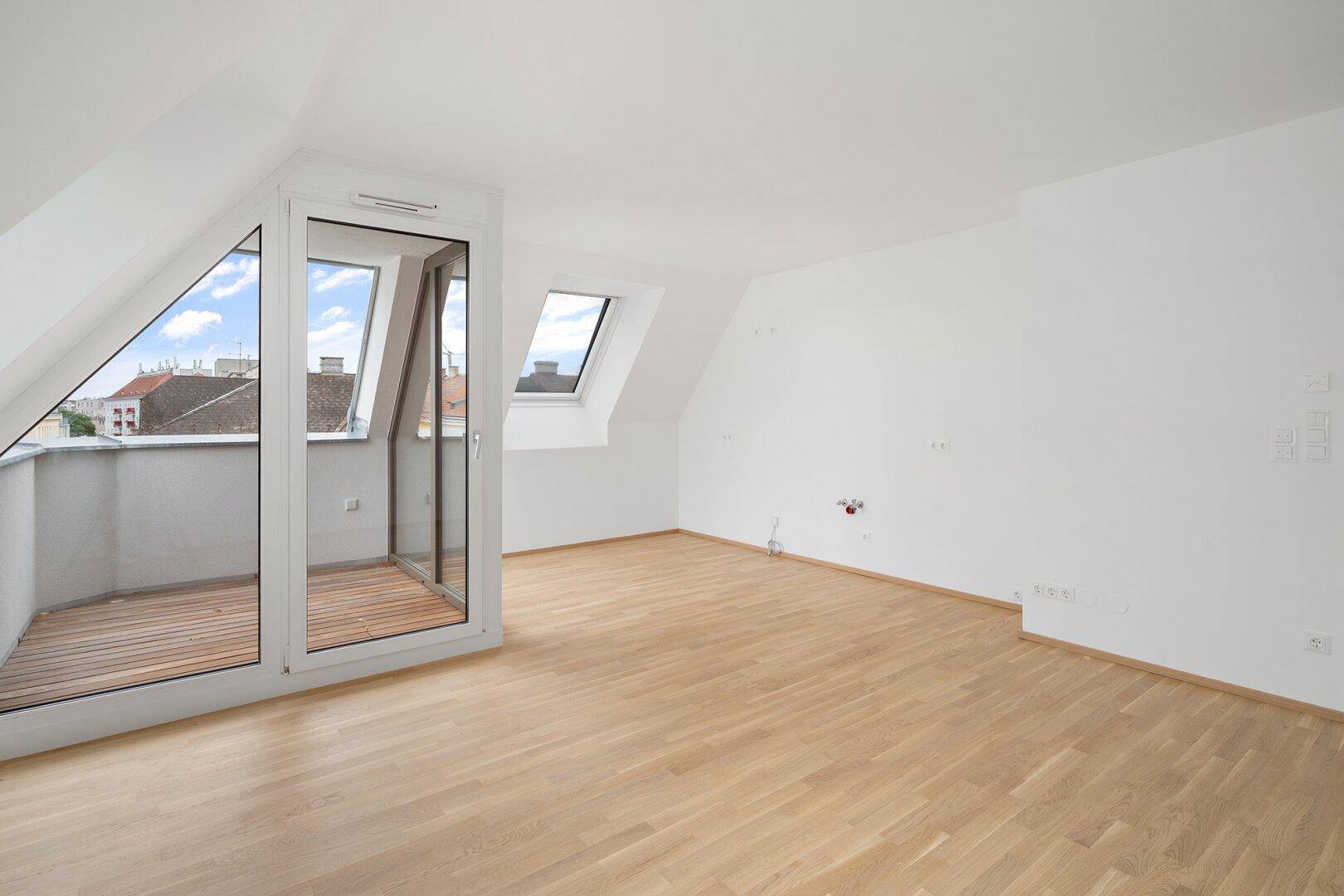 Helles Dachzimmer mit Holzboden, Dachfenstern und einer Loggia mit Blick über die Dächer.