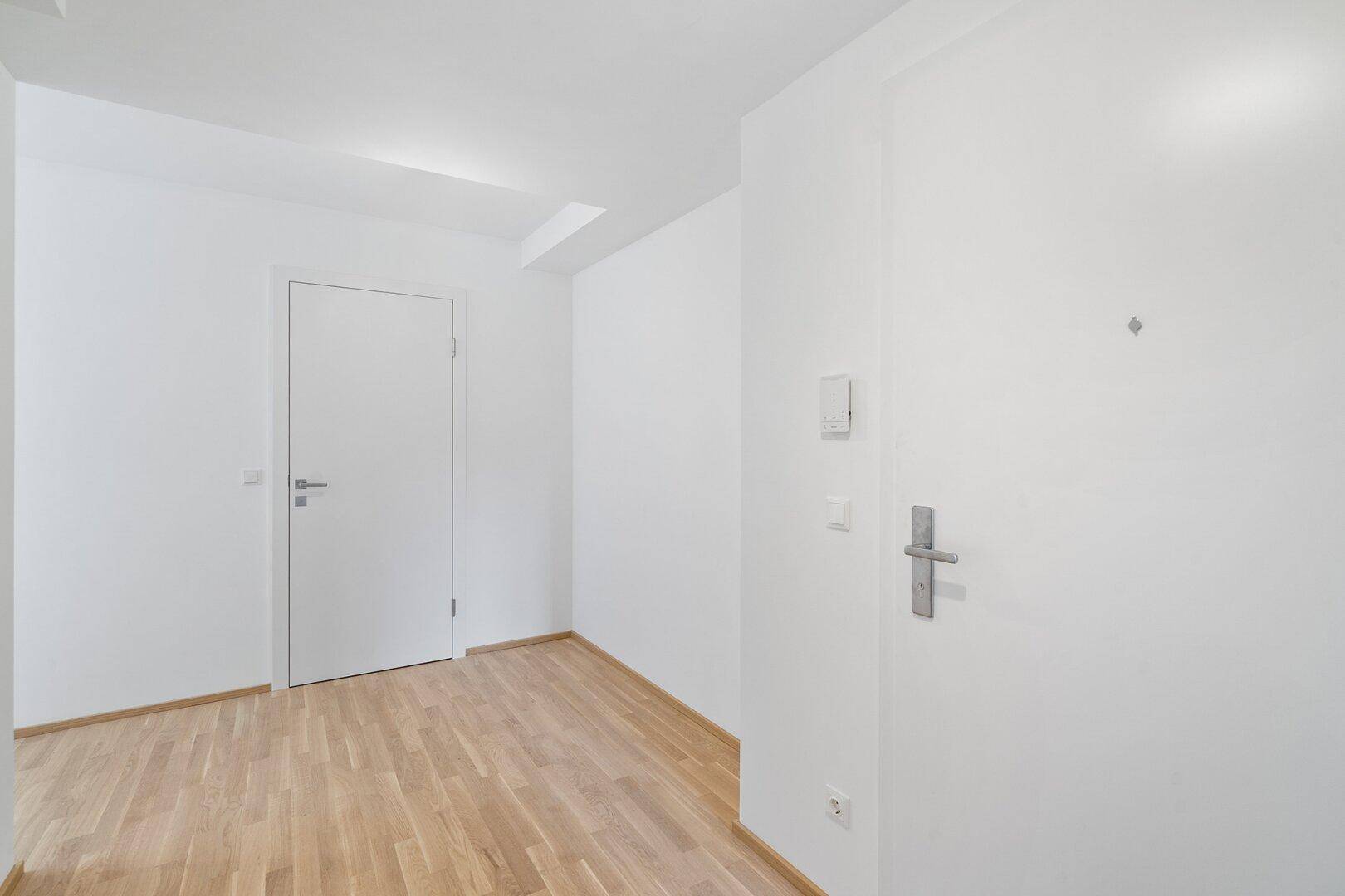 Moderner Eingangsbereich einer Wohnung mit hellem Holzboden und weißer Innentür.