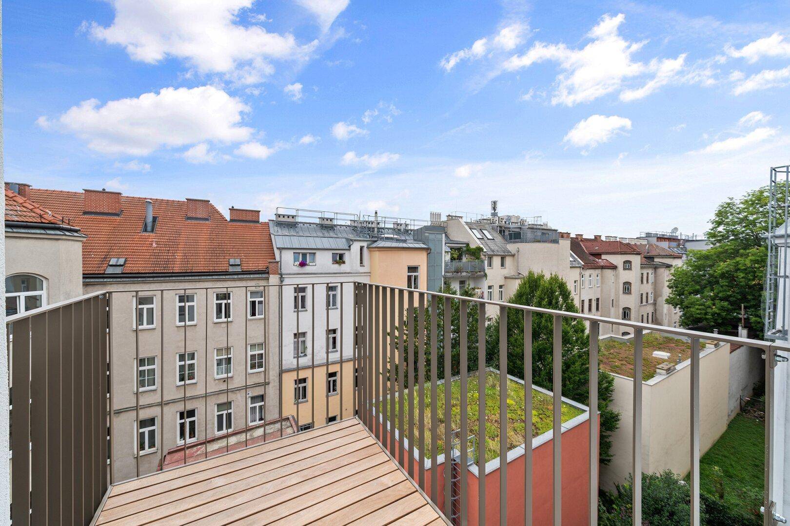 Kleiner Balkon mit Holzboden und Blick auf die umliegenden Dächer und die Stadt.