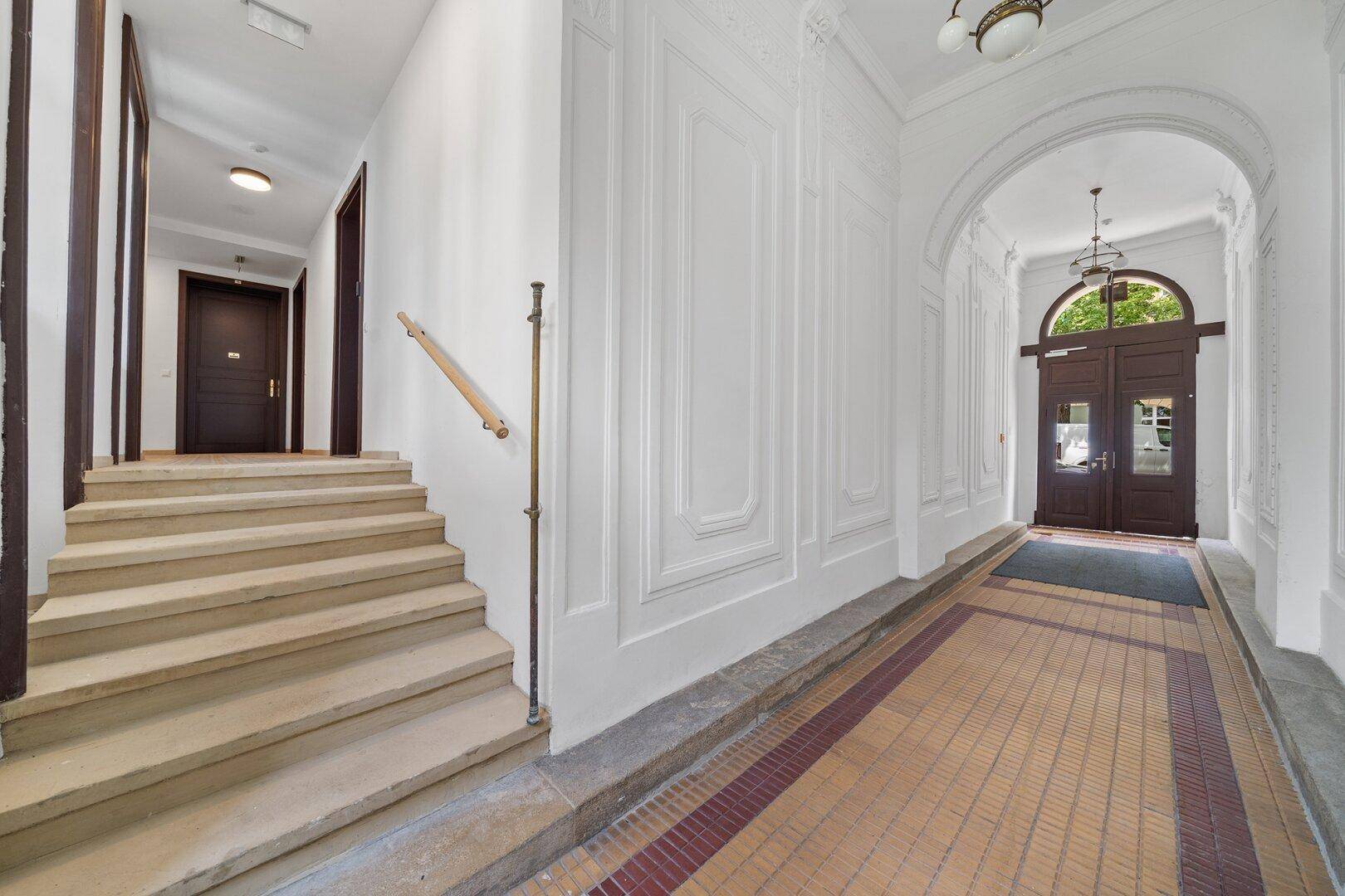 Elegantes Entrée eines Altbaus mit Stuckelementen, Fliesenboden und hohen Decken.