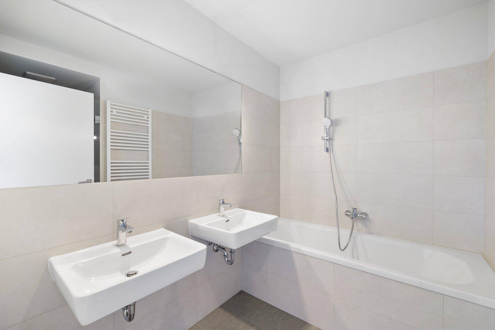 Modernes Badezimmer mit zwei Waschbecken, Badewanne, großem Spiegel und beheiztem Handtuchhalter.