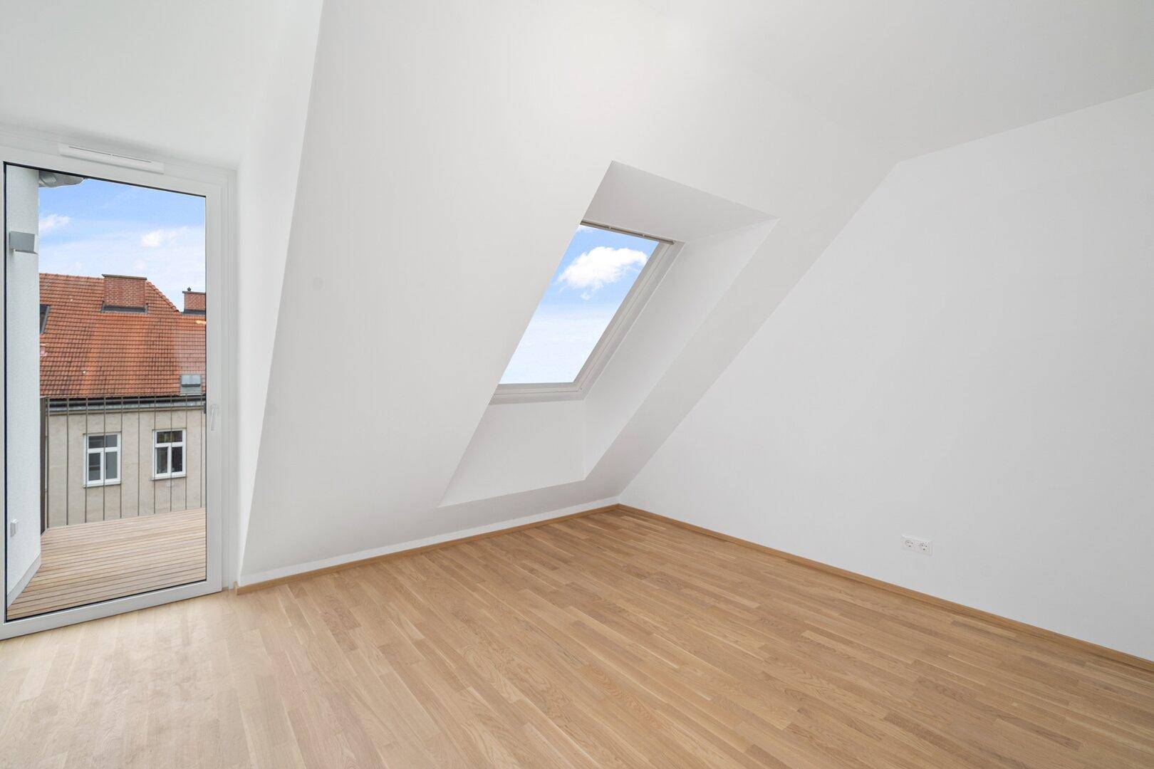 Helles Dachgeschosszimmer mit Holzboden, Dachfenster und direktem Zugang zur Terrasse.