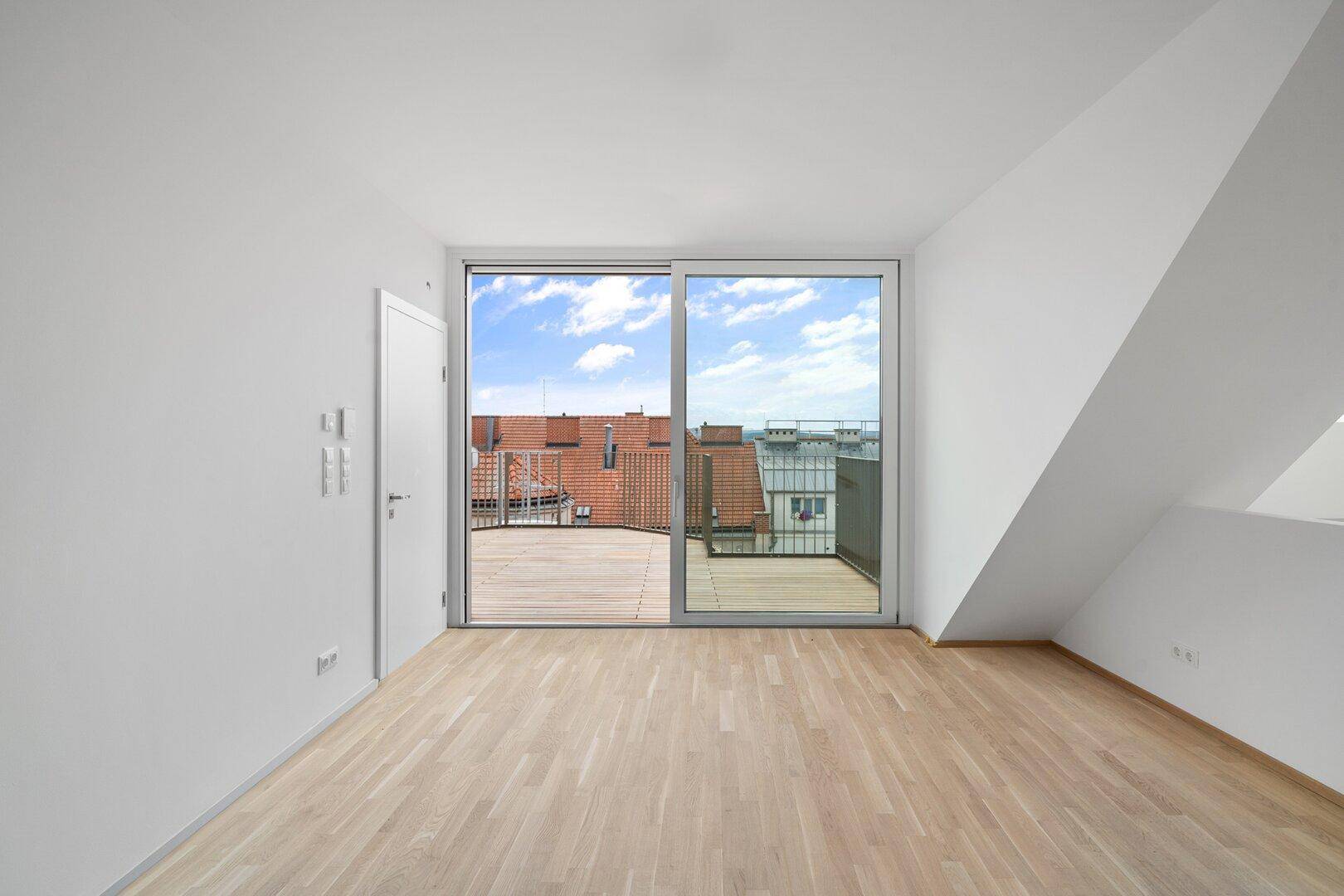 Geräumiges Dachgeschosszimmer mit Holzboden und großzügigem Zugang zur Dachterrasse.