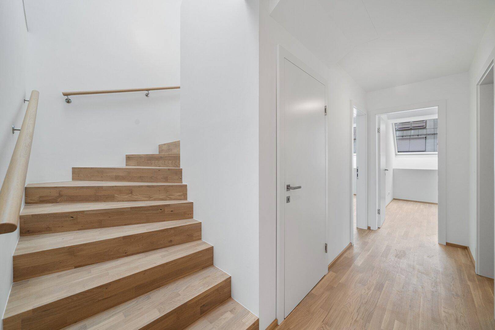 Heller Flur mit moderner Holztreppe und Holzboden, der zu den oberen Etagen führt.