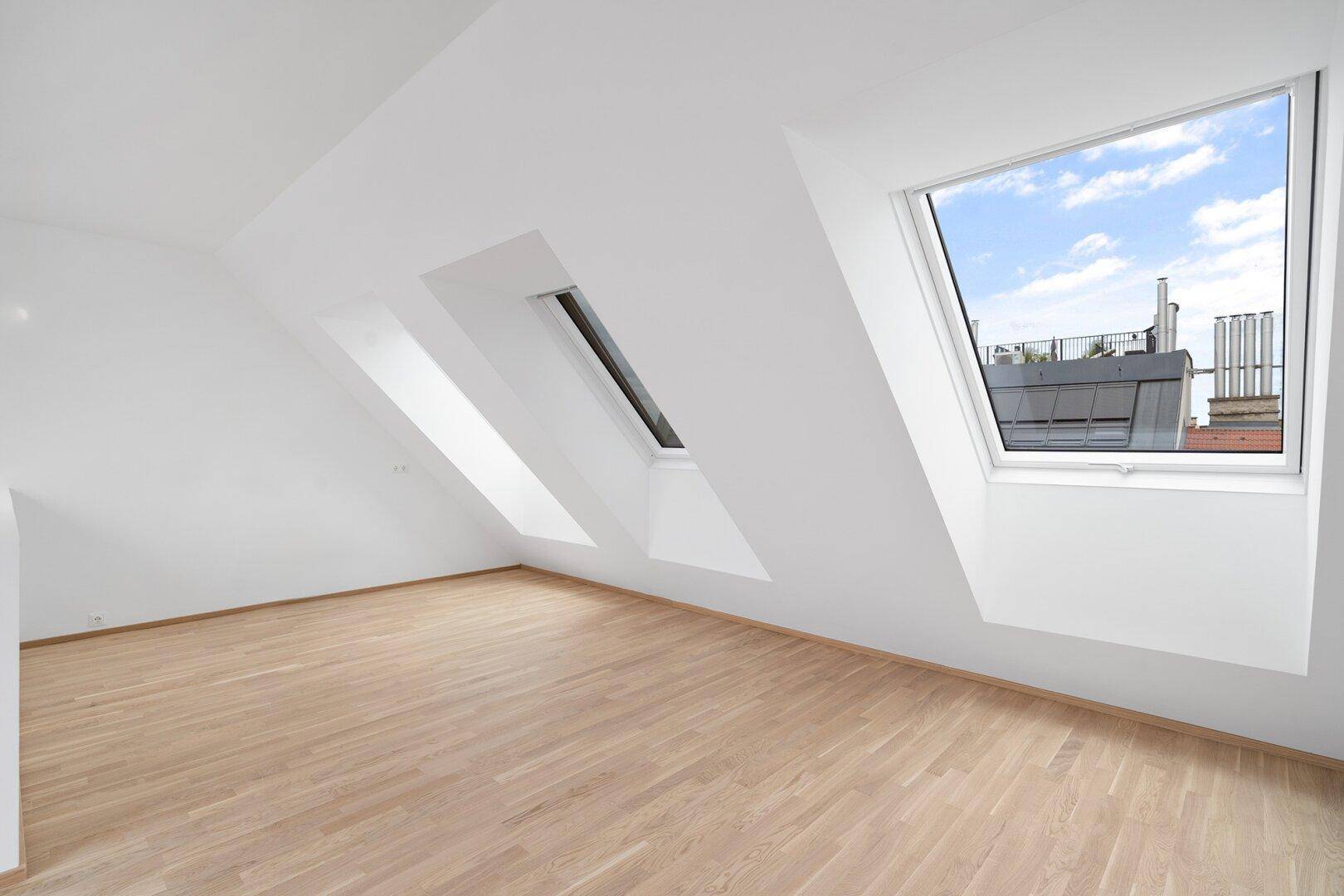 Helles Dachgeschosszimmer mit Holzboden, weißen Wänden und mehreren Dachfenstern.