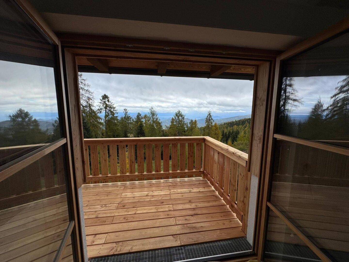 Geräumiger Holzbalkon mit weitem Blick auf die bewaldete Berglandschaft unter einem bewölkten Himmel.